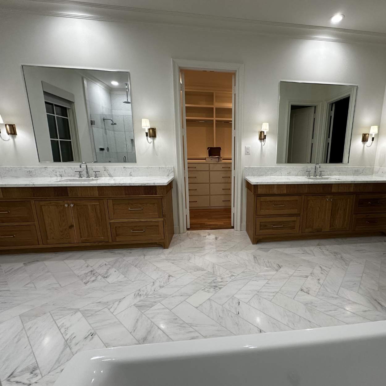 Bathroom with double vanity mirrors, marble countertops, wooden cabinets, and a walk-in shower in the background.