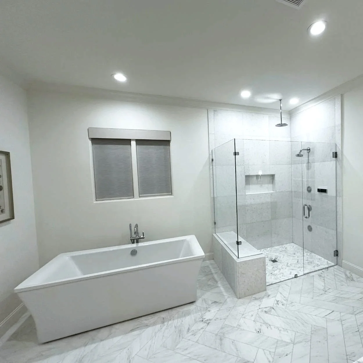 Modern bathroom with a white bathtub, a glass-enclosed shower with gray tiles, and marble-patterned flooring.