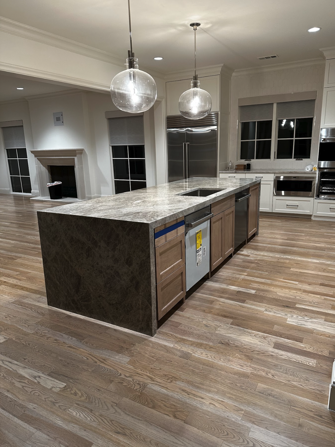 Modern kitchen with a large island, marble countertop, wooden cabinets, stainless steel appliances, hardwood floors, and pendant lighting.