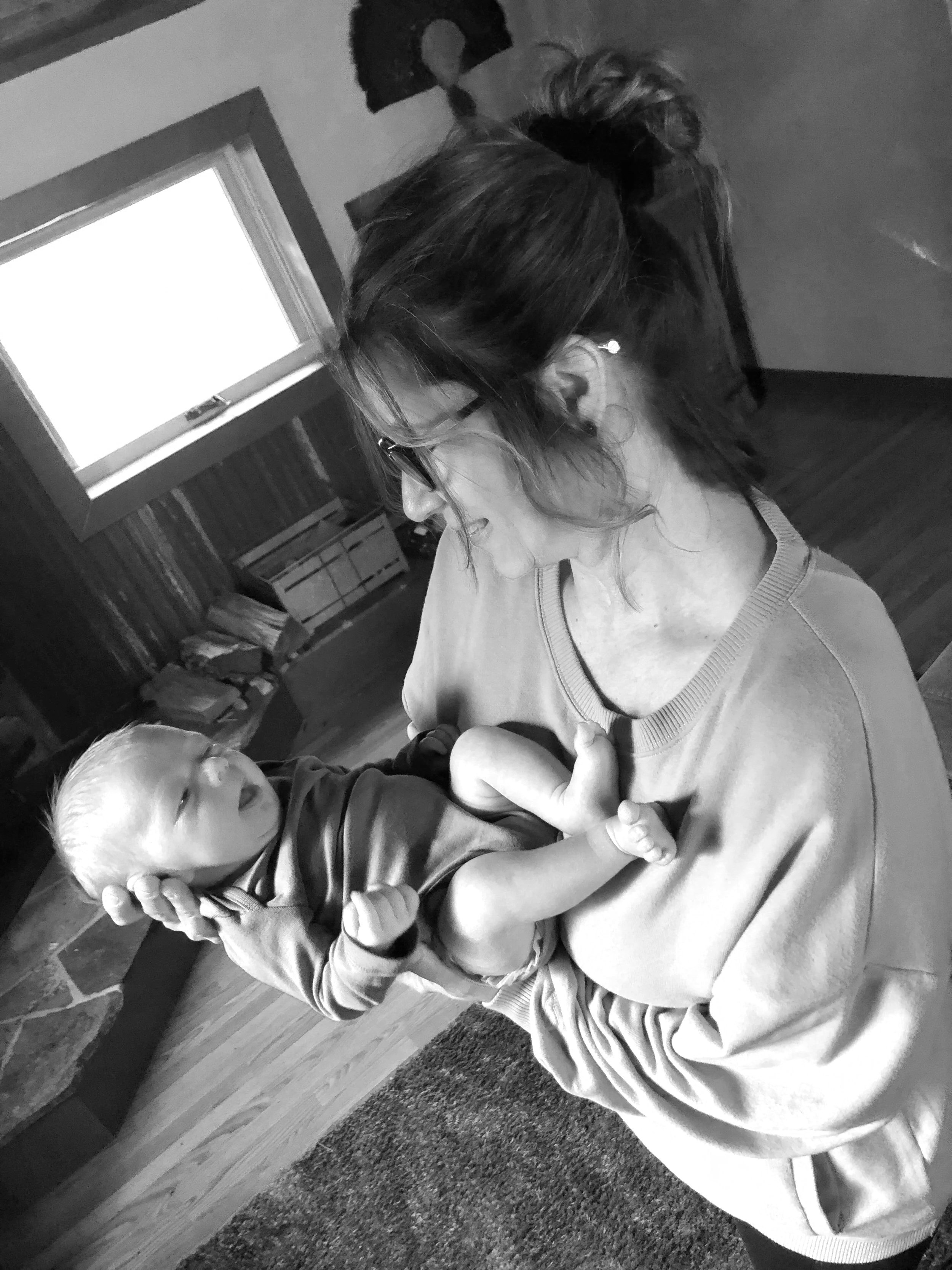 A woman with glasses holding a baby in her arms indoors.