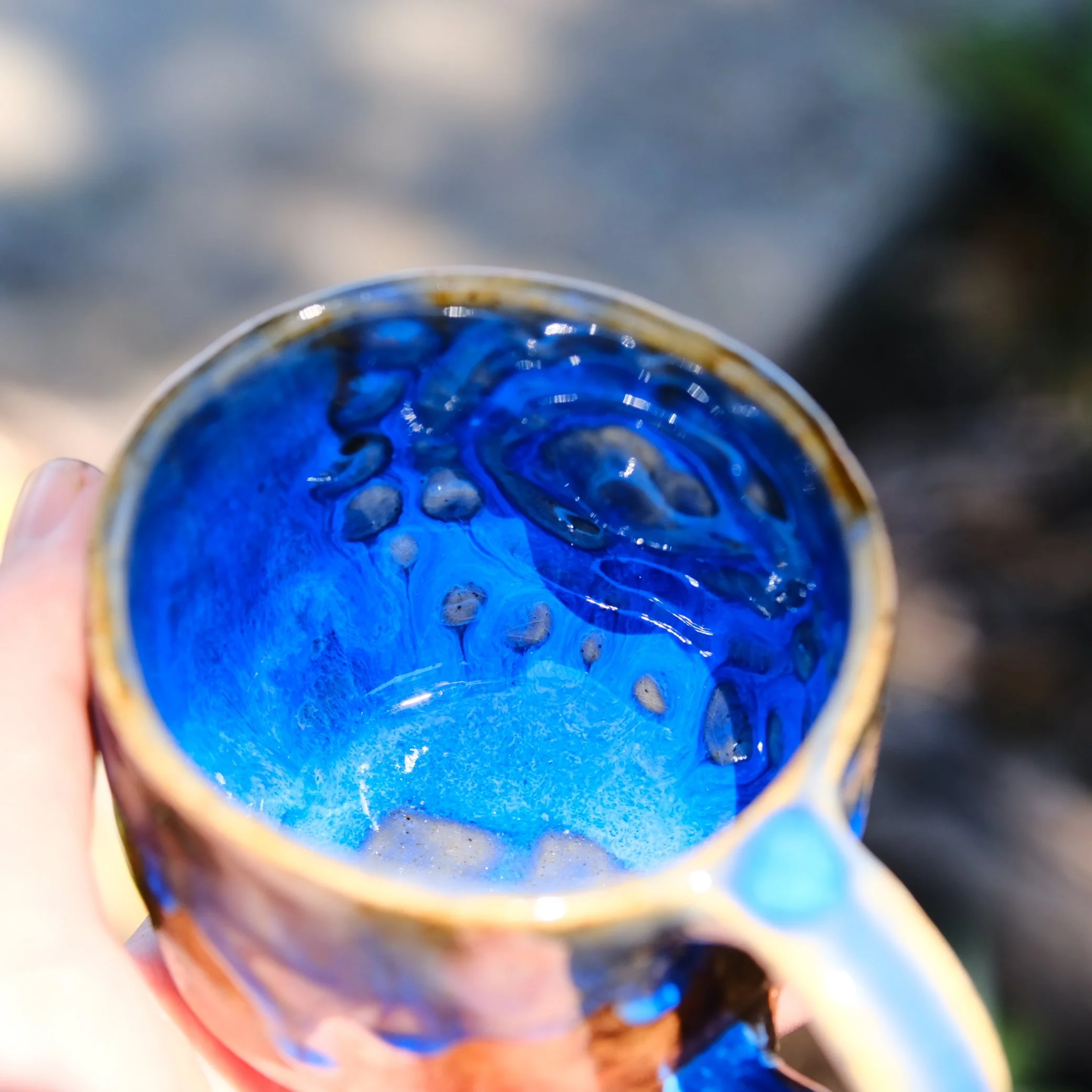 Profile of a rustic, spirit-inspired pottery mug showing the blue-glaze accents and hand-formed handle.