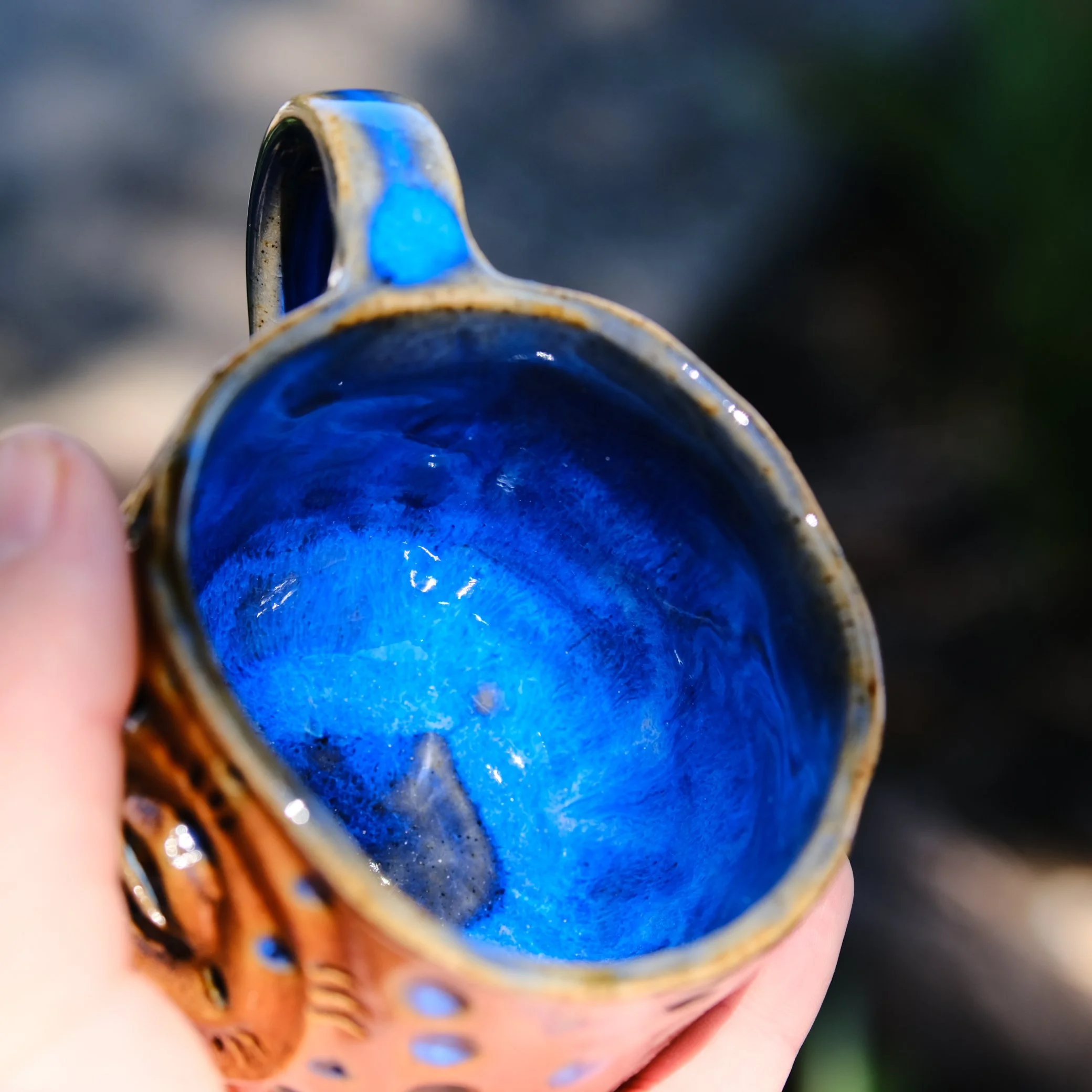 Deep blue cosmic glaze inside a handmade tribal mug, contrasting with the raw, textured exterior.