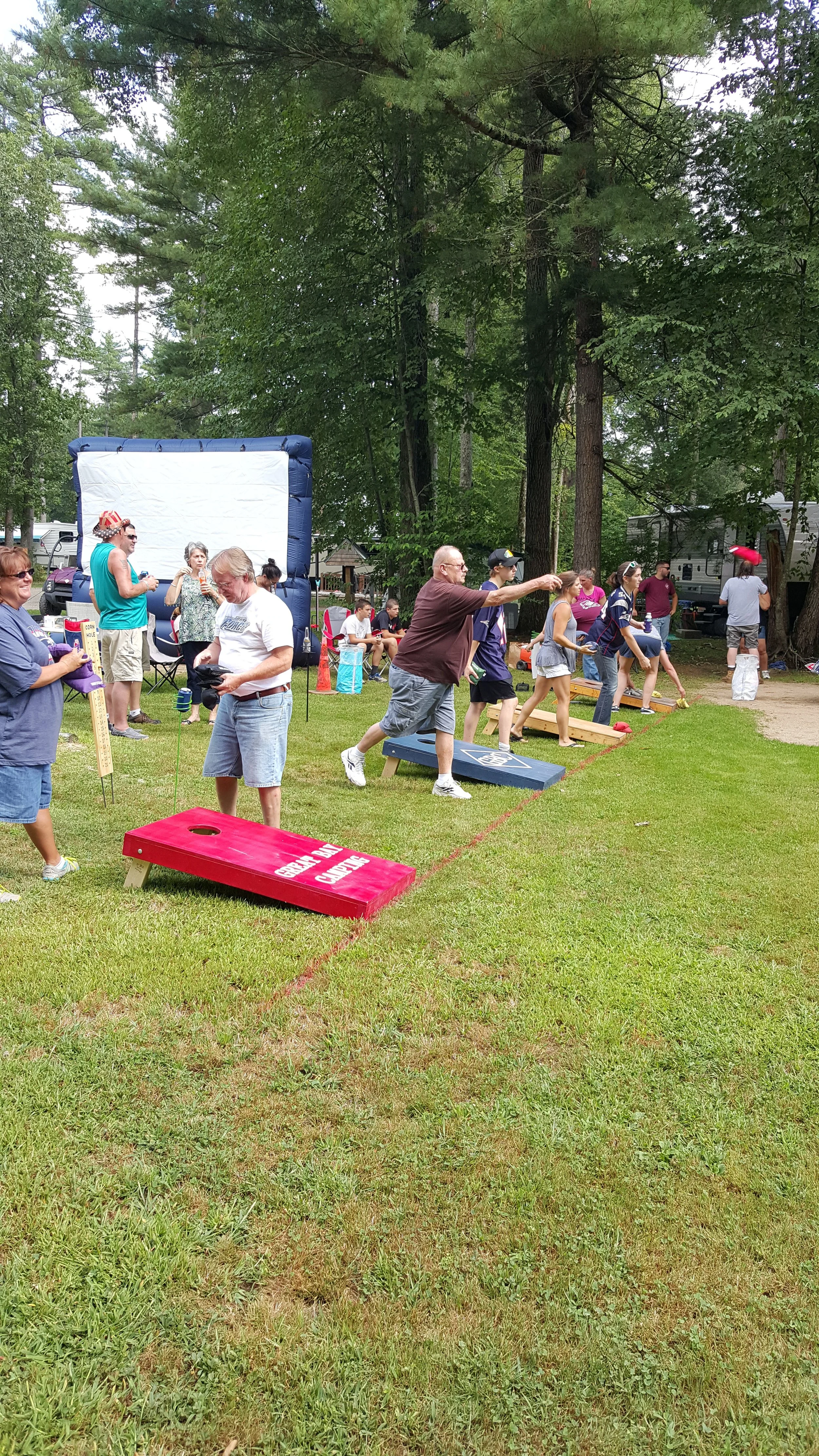 People playing cornhole at an outdoor gathering with tents and trees in the background.