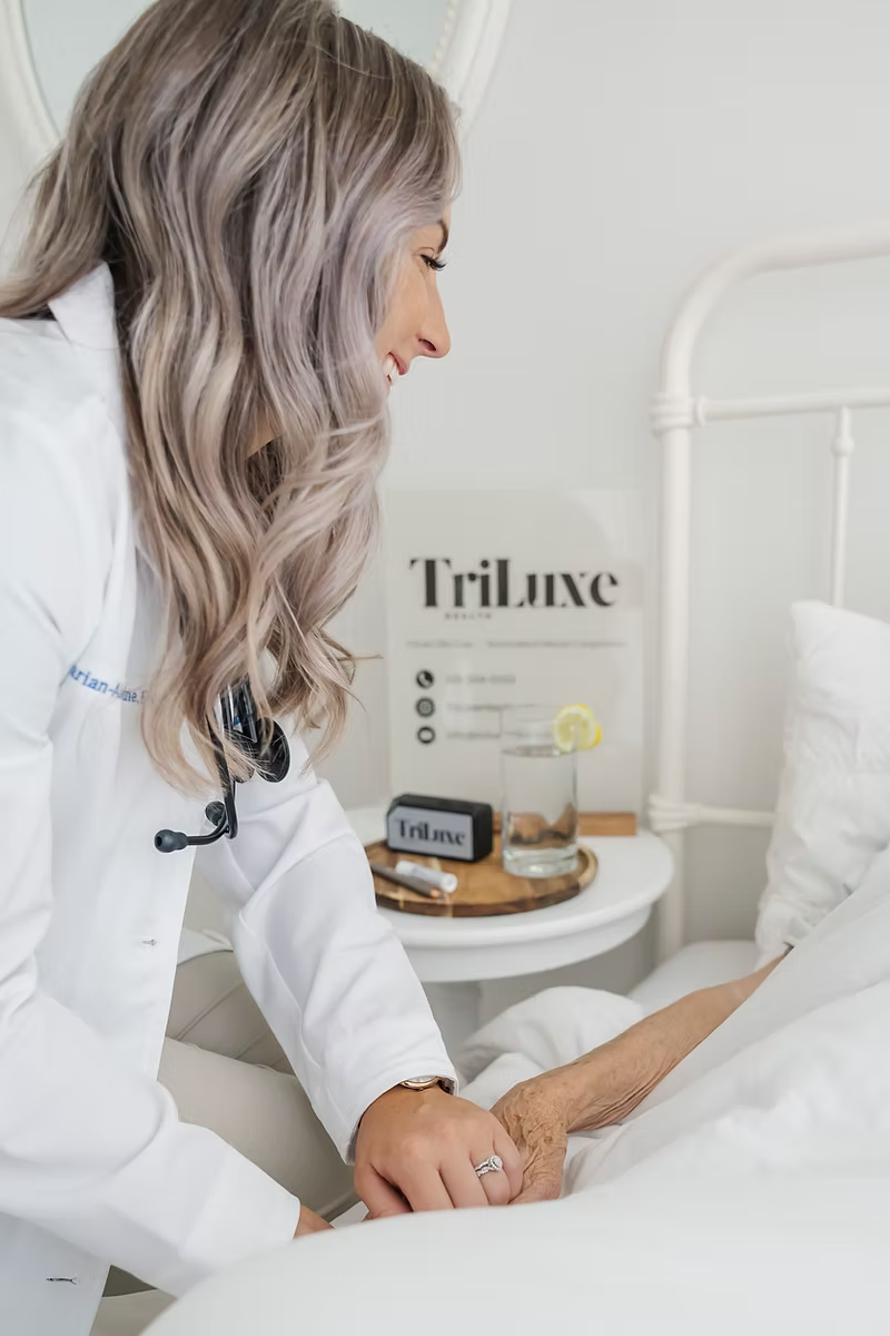 A female healthcare professional holding an elderly patient's hand in a white bedroom.