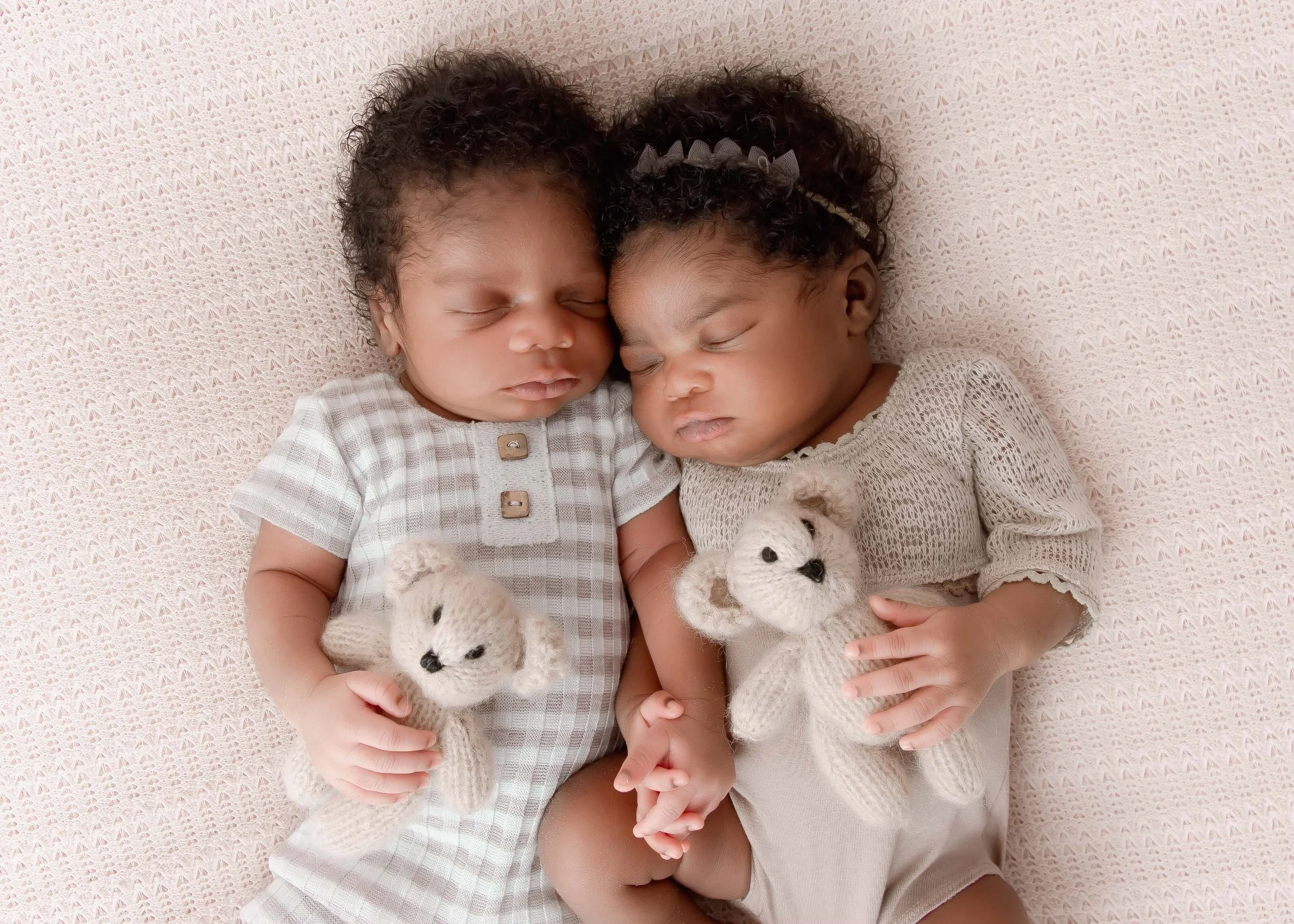 Two sleeping babies holding small teddy bears while lying on a pink blanket.