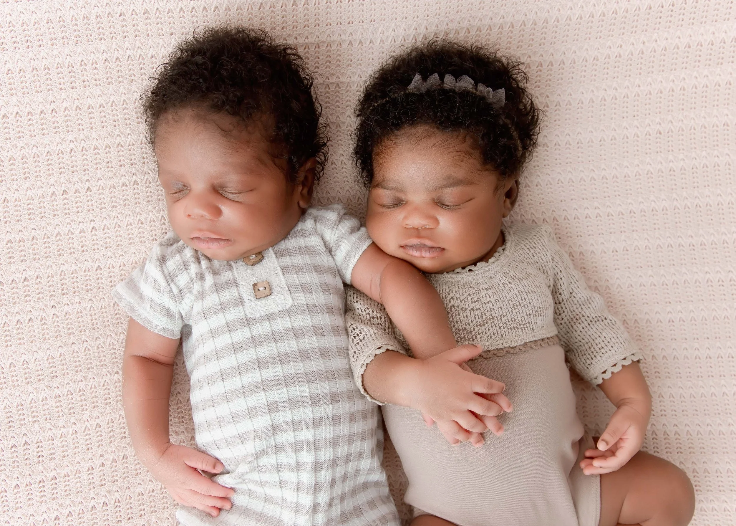 Two sleeping African-American babies lying on a pink woven blanket, holding hands.
