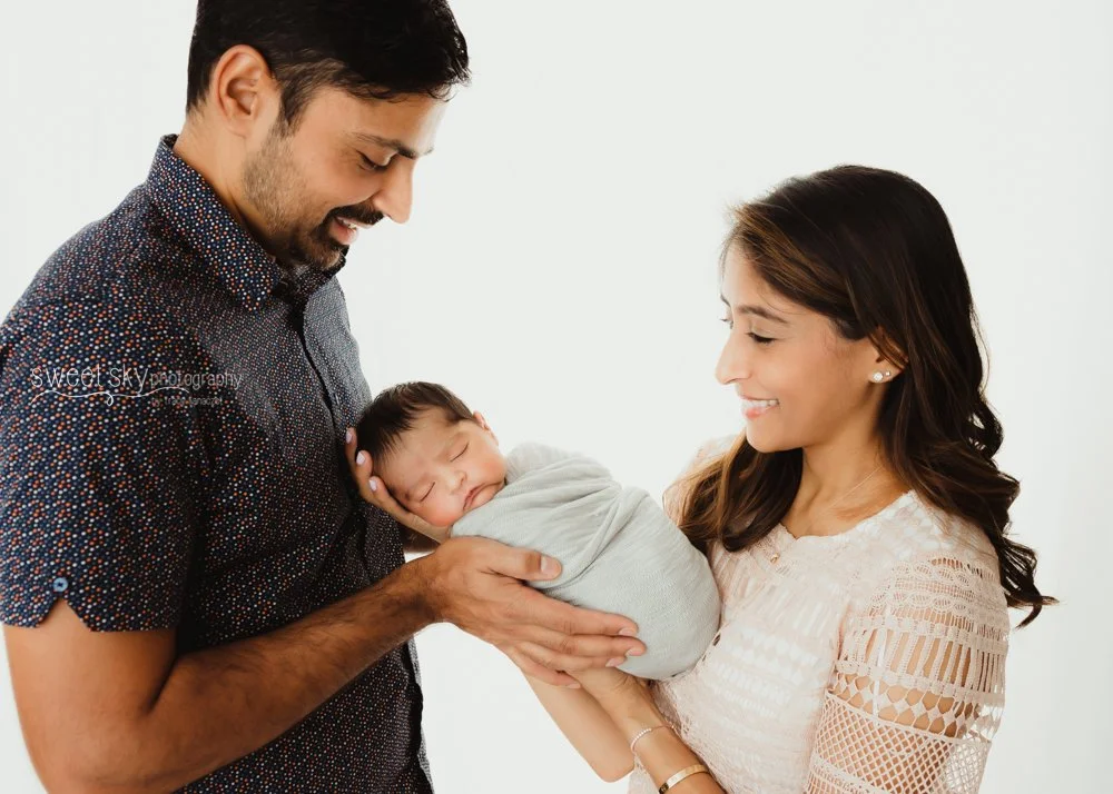Happy couple holding their newborn baby, smiling at each other, in a bright setting.