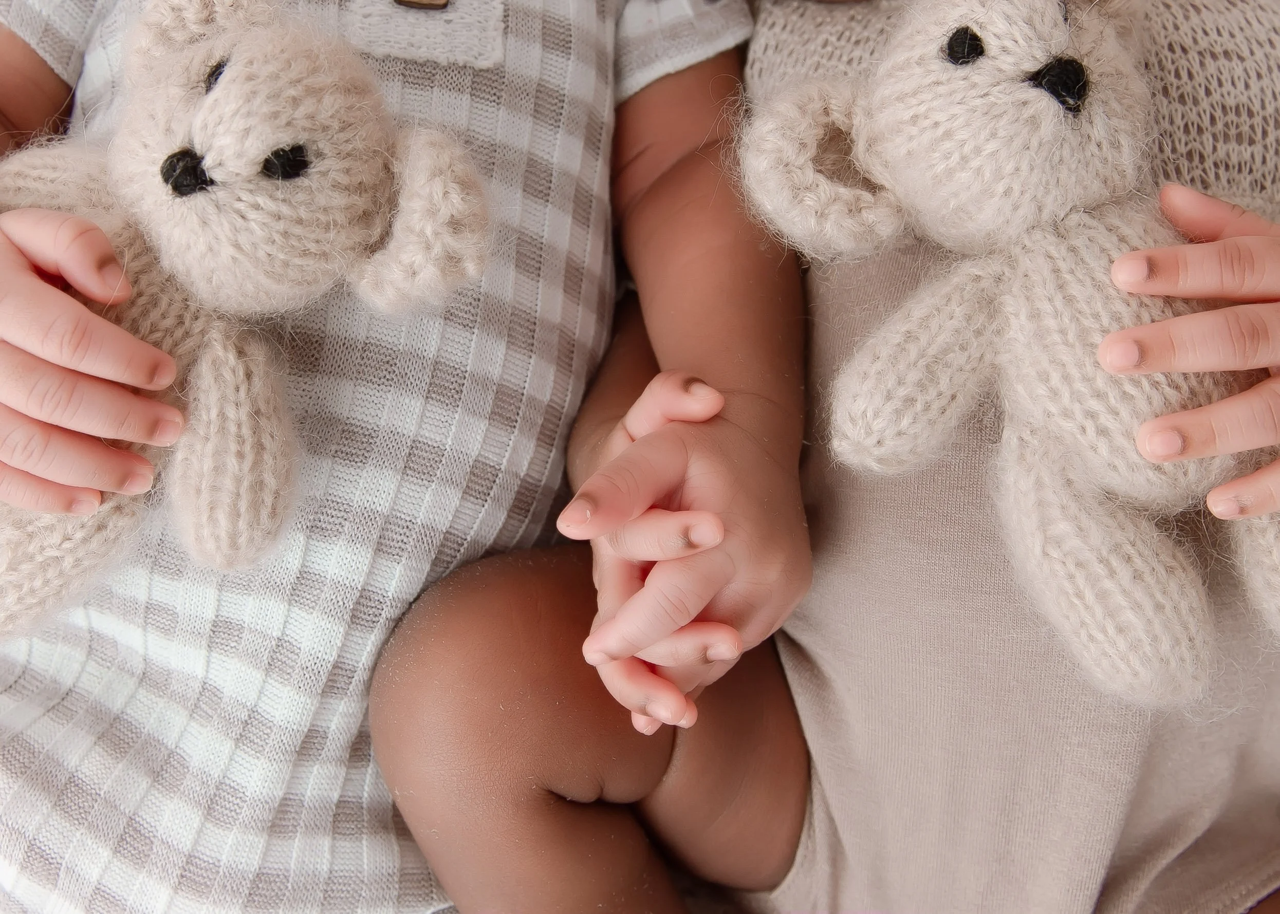 Two children holding knitted teddy bears on their laps, with their hands clasped together.