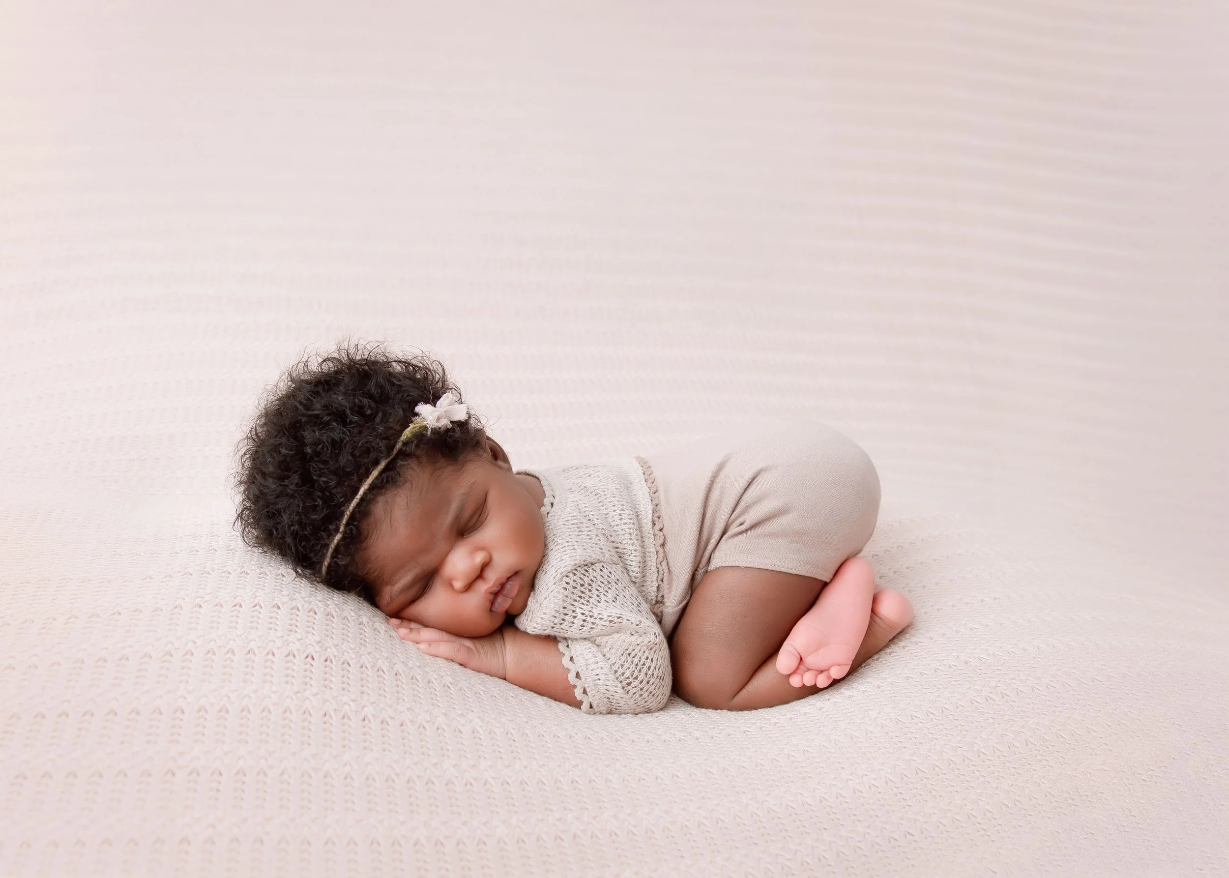 A young girl with curly hair and a headband sleeping on a soft, light-colored blanket.