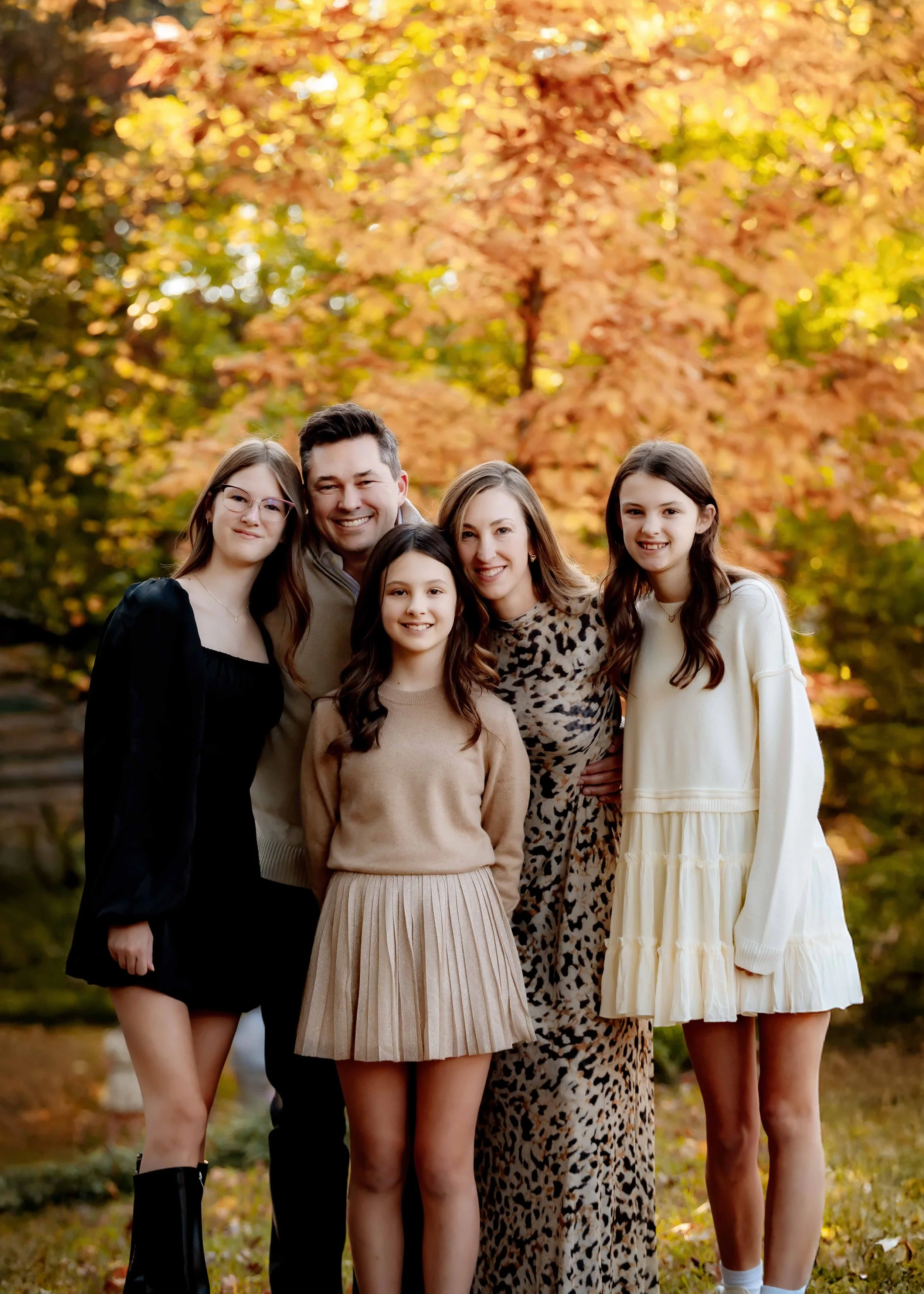 Family of five posing outdoors in autumn with colorful fall foliage in the background.