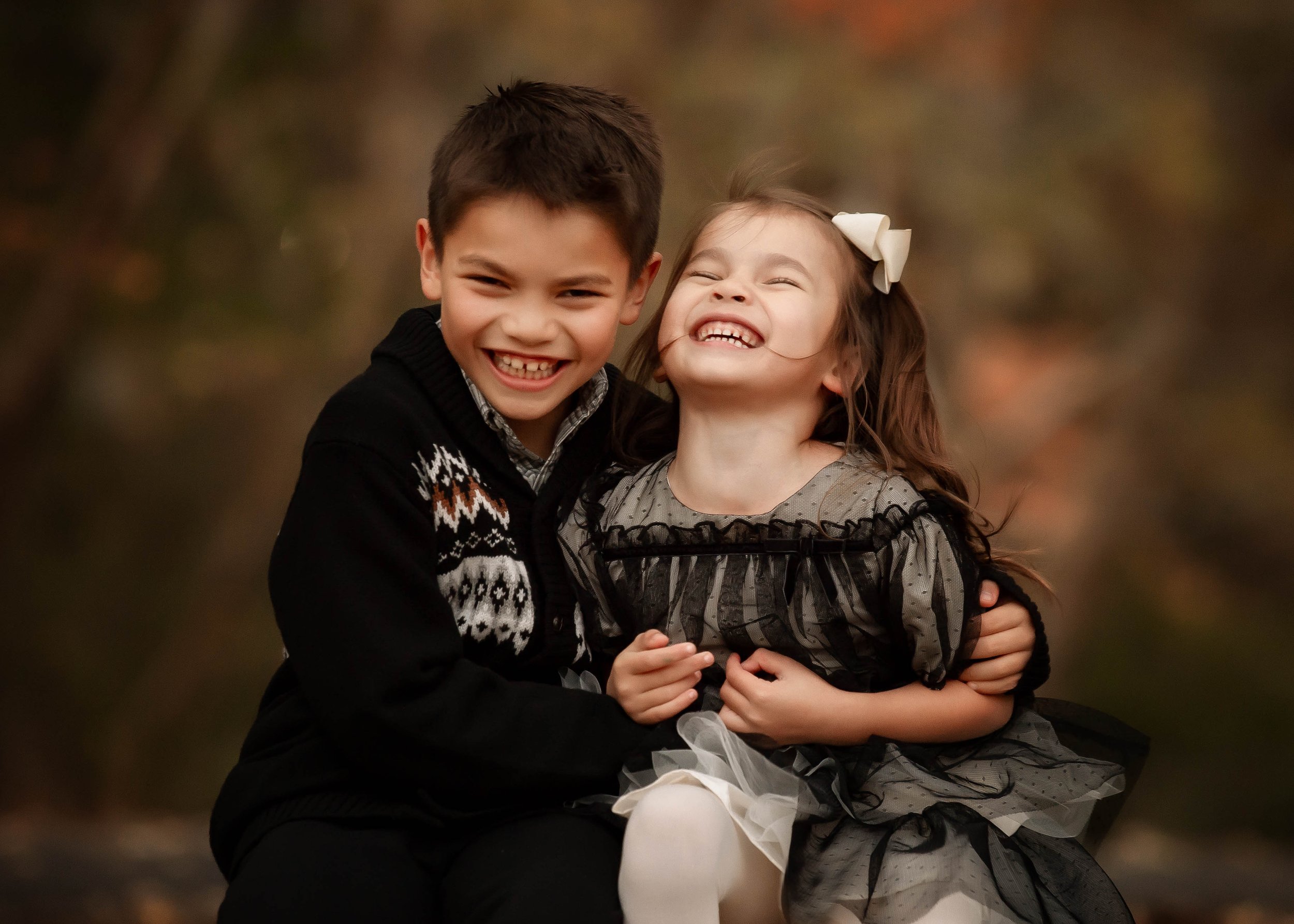 A young boy and girl sitting outdoors, smiling and laughing, embracing each other in a joyful moment.