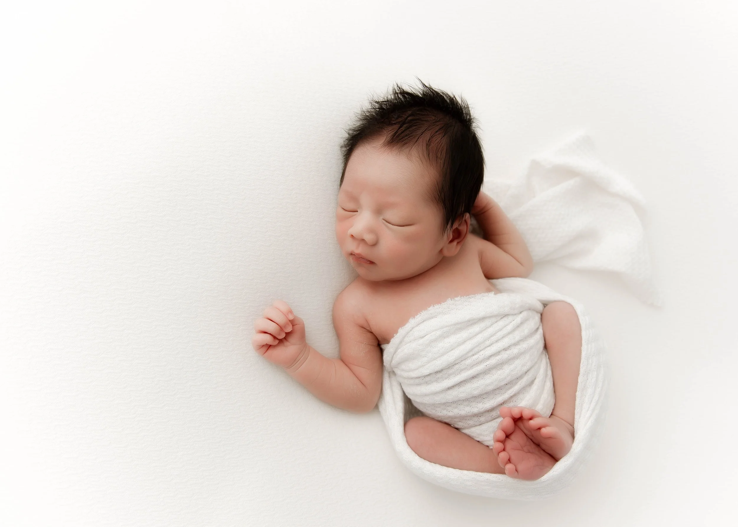 Sleeping newborn baby wrapped in a white towel on a white background.