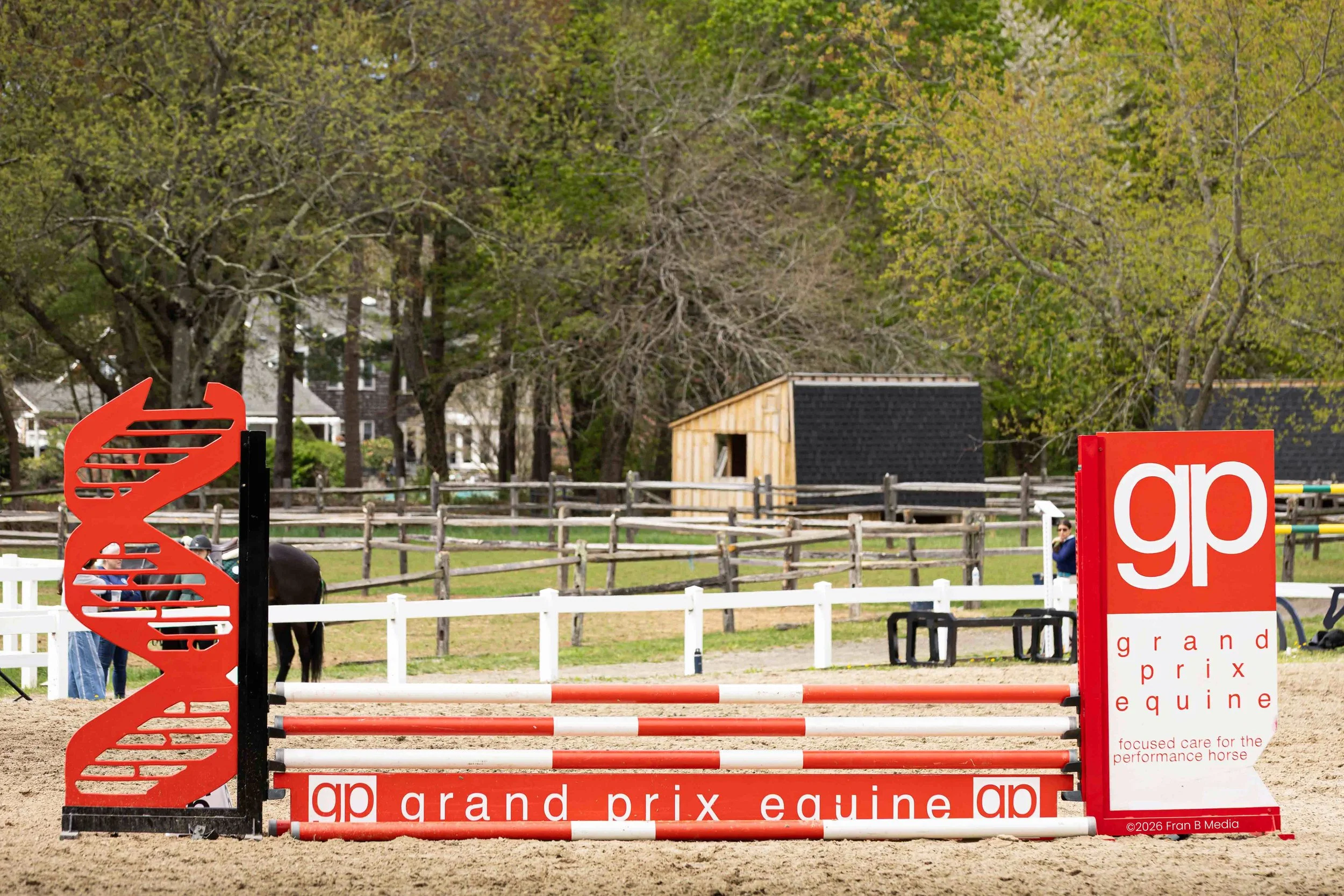 Horse jumping obstacle at a horse riding competition with trees and houses in the background.