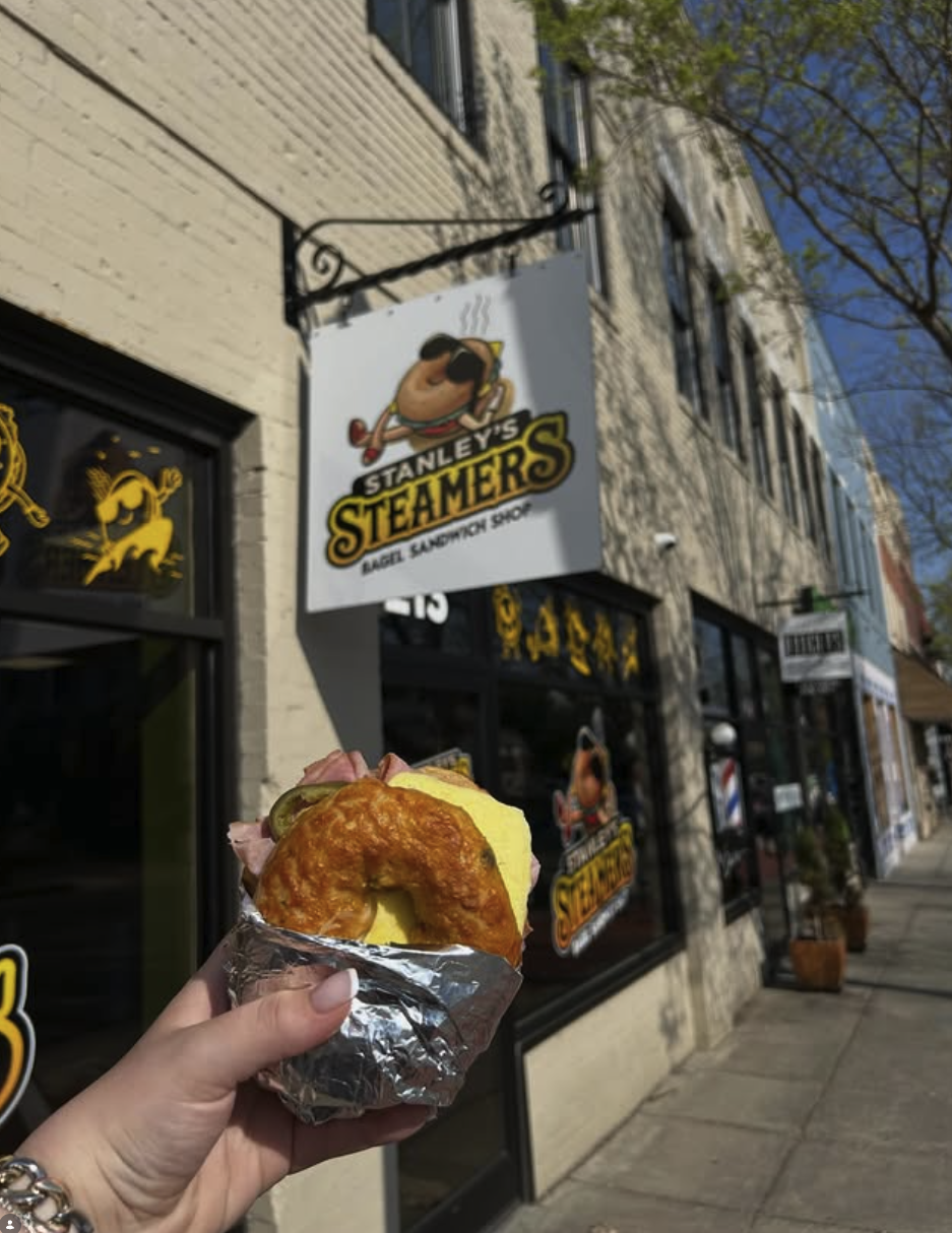 A person holding a fish sandwich wrapped in aluminum foil outside Stanley's Steamers bagel sandwich shop.