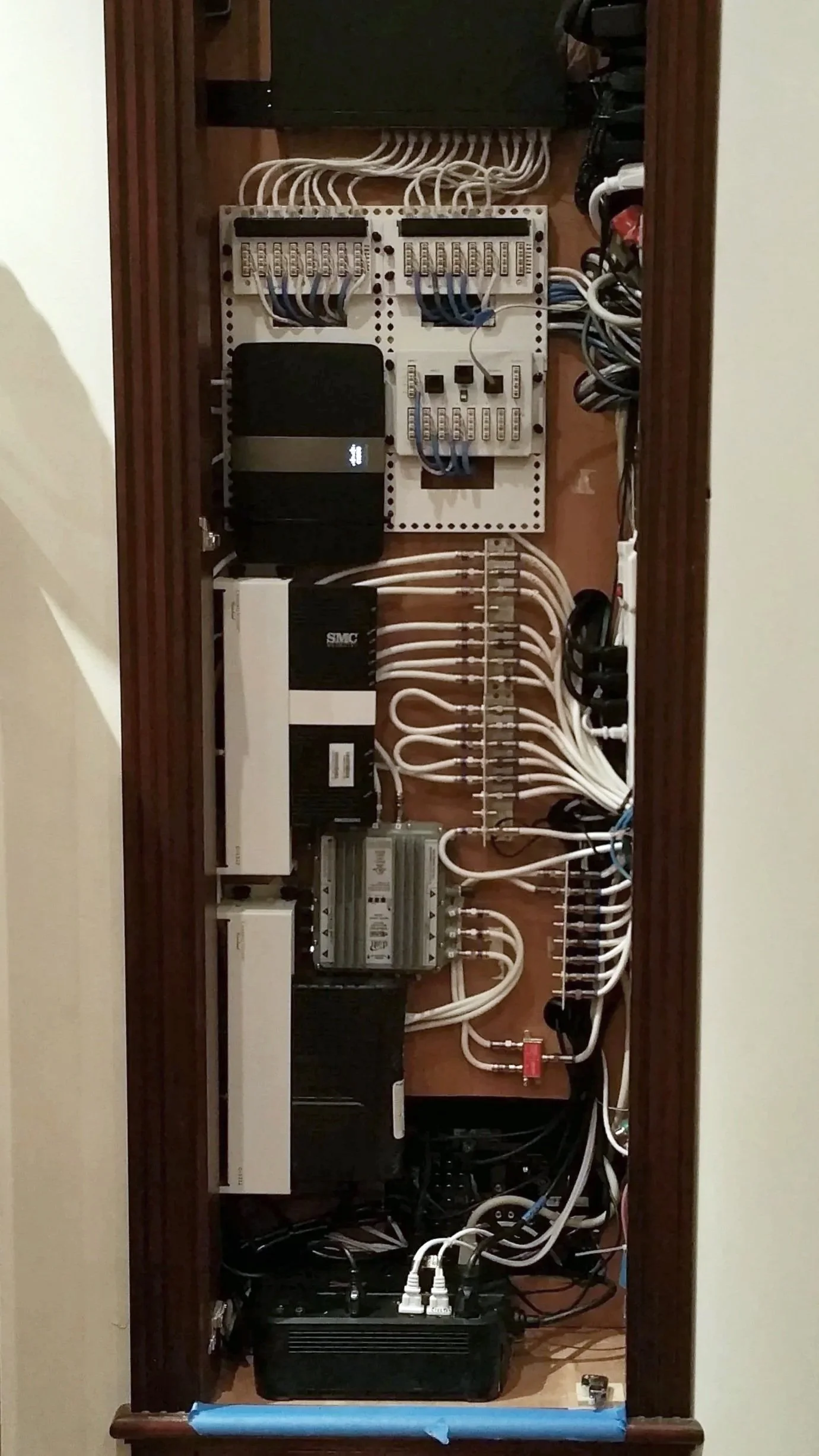 An electrical or networking panel with various wires, circuit breakers, and electronic devices installed inside a wooden frame