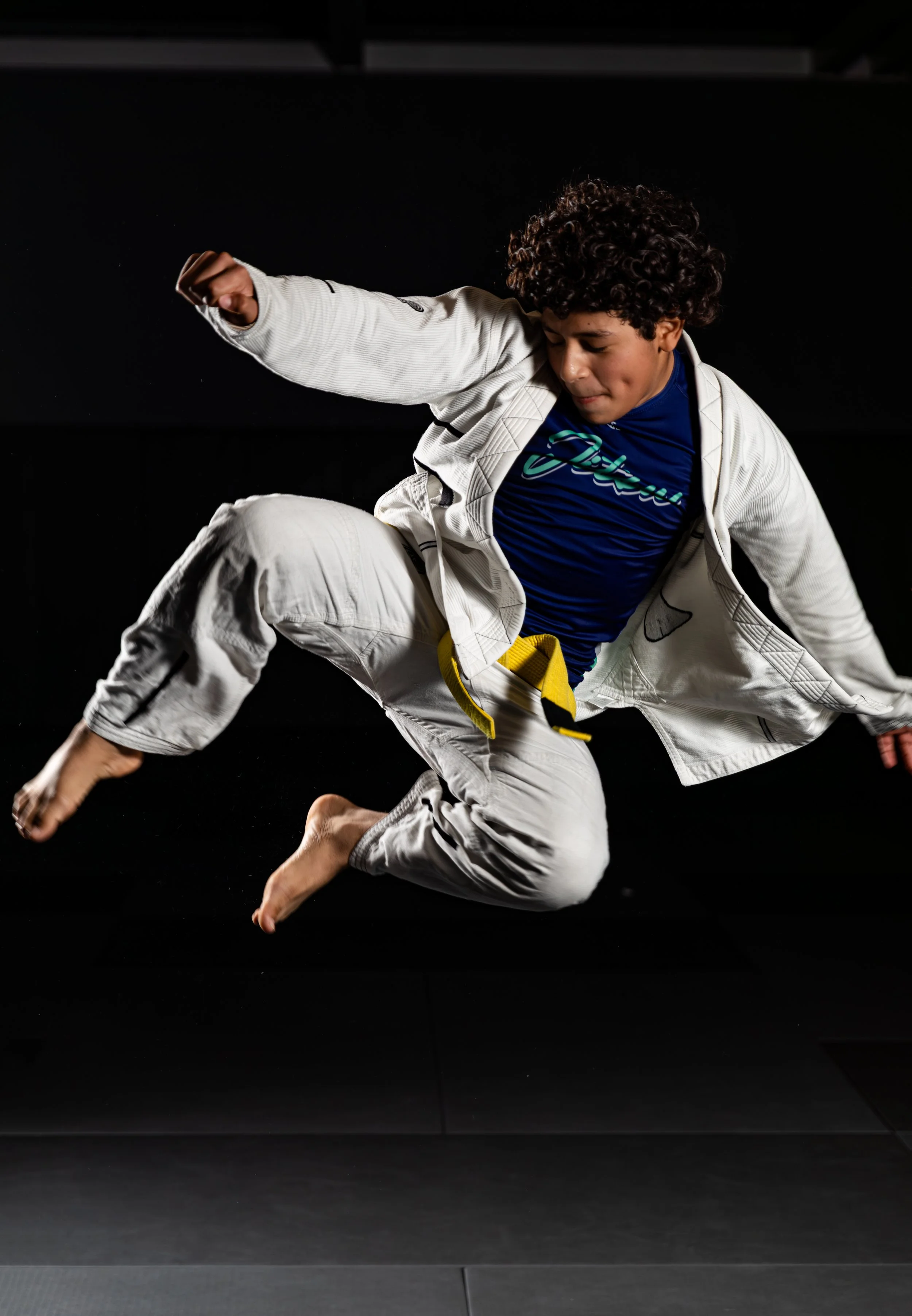 Young man in white martial arts gi falling or tumbling against a black background