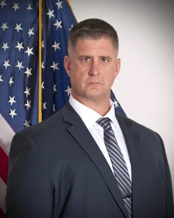 A man in a suit standing in front of an American flag.