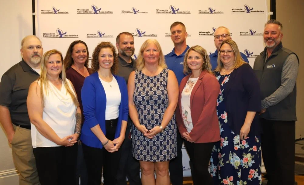 Group of ten people standing in front of a backdrop with Wisconsin Correctional Association logos, posing for a group photo at an indoor event.