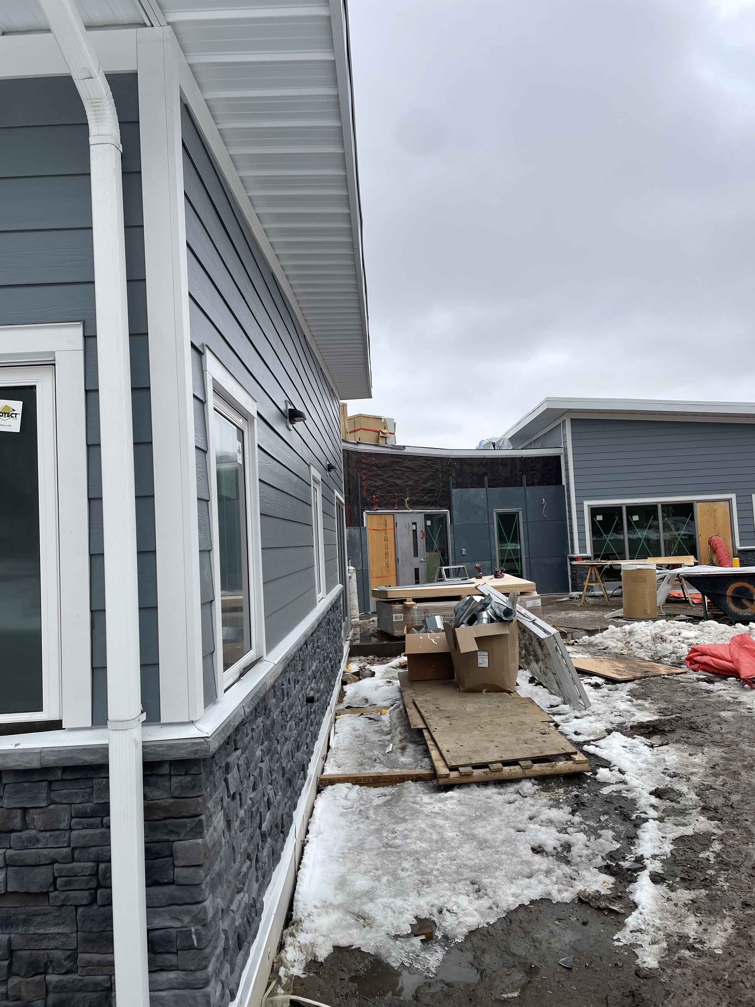 Construction site with partially built houses, cardboard boxes, and scattered building materials on snow and muddy ground.