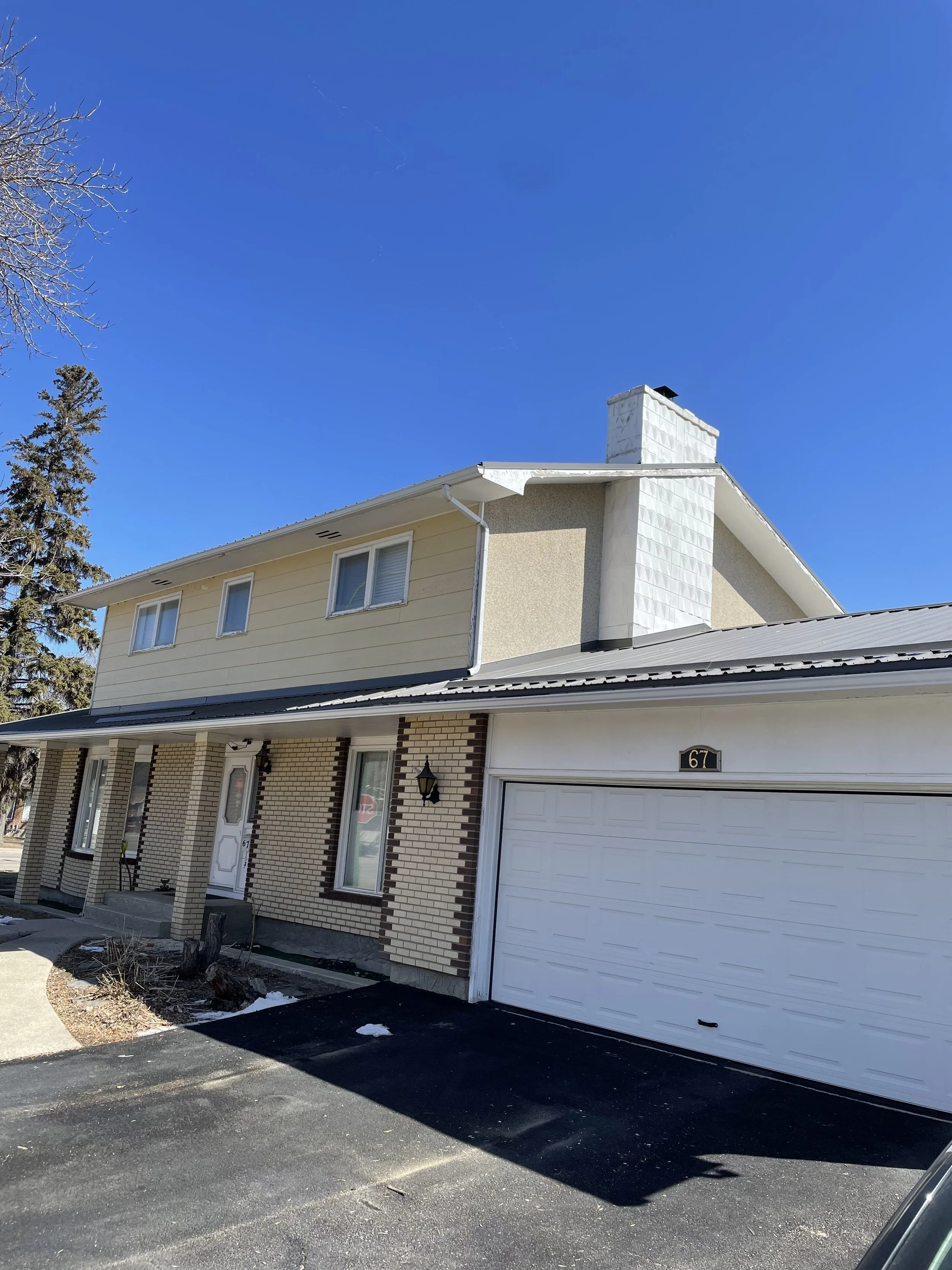 A two-story house with brick and siding exterior, a garage door, a front porch with steps, and a chimney under a clear blue sky.