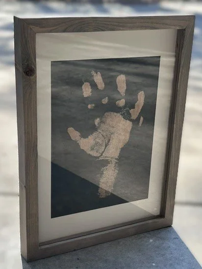 Framed print of a handprint with five fingers, outdoors on snowy ground.