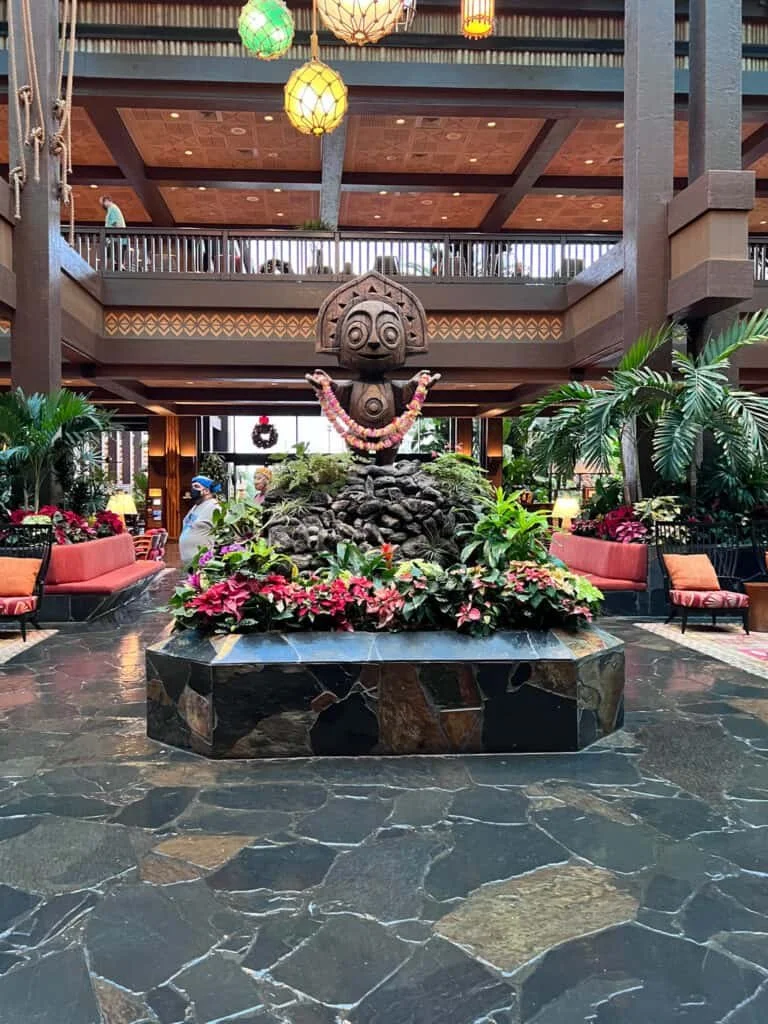 Main lobby of Disney's Polynesian Village Resort featuring the iconic tiki statue and tropical plants.
