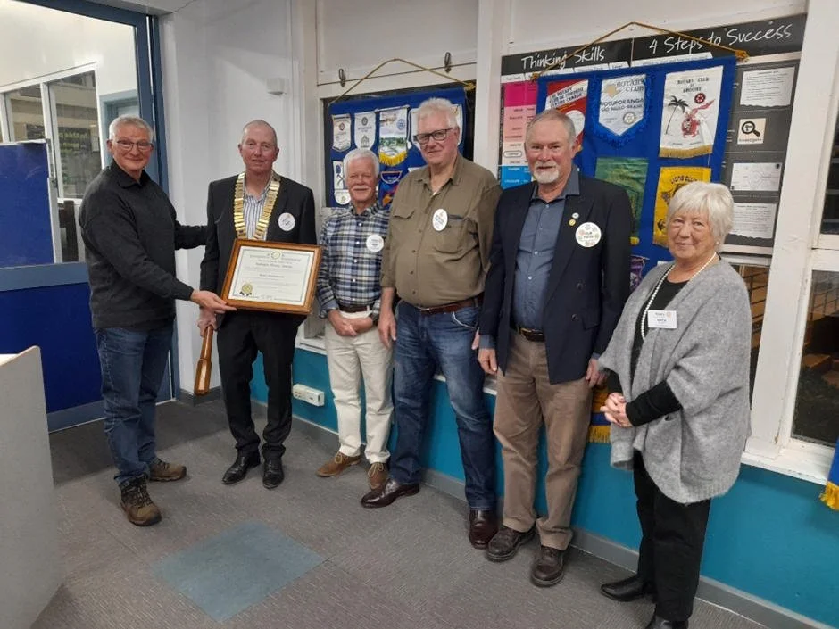 Six people standing inside a room, one holding a framed certificate, with a bulletin board and a sign reading "Thinking Skills: 4 Steps to Success" on the wall behind them.