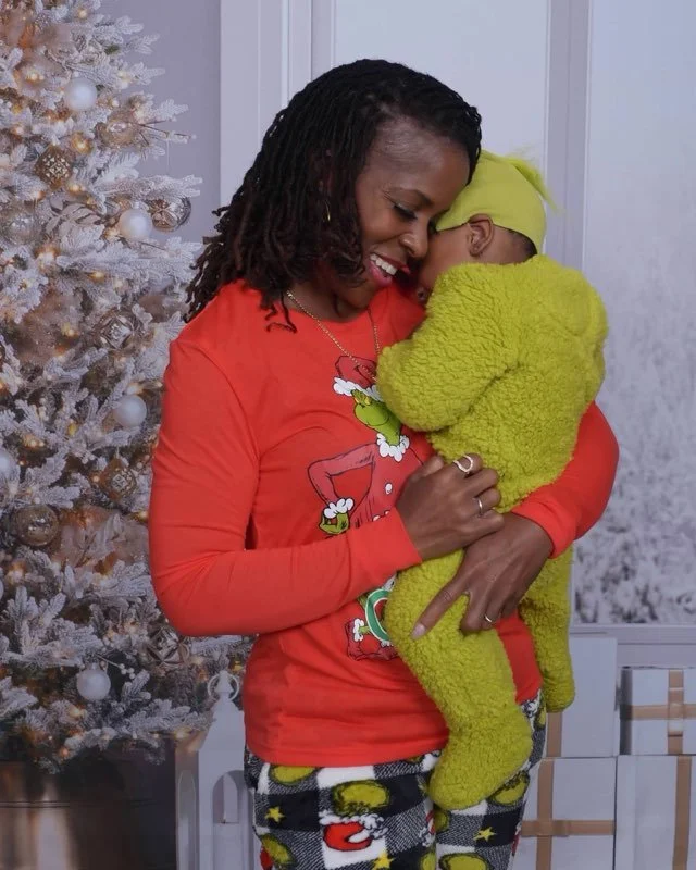 A woman and a baby sharing a hug with their foreheads touching in front of a decorated Christmas tree.