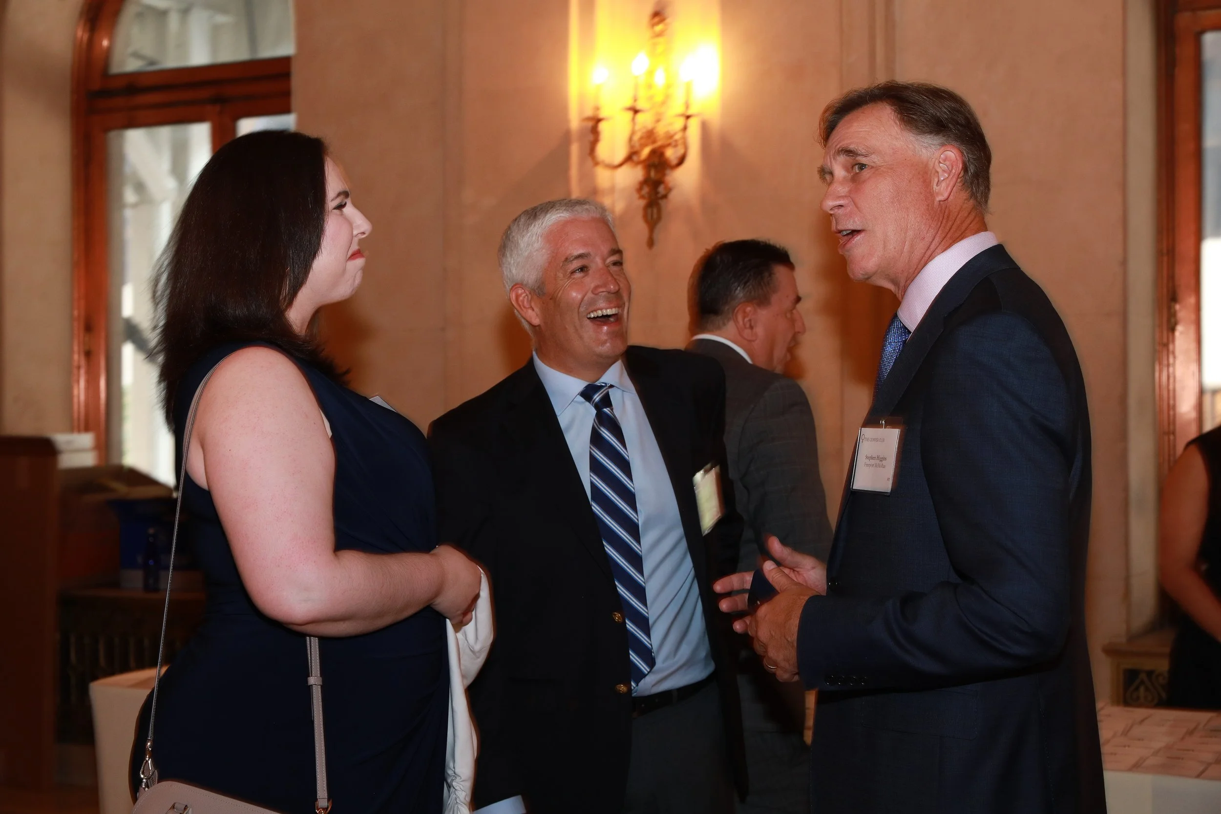 Four people engaged in conversation at a formal event in an elegant room with warm lighting.