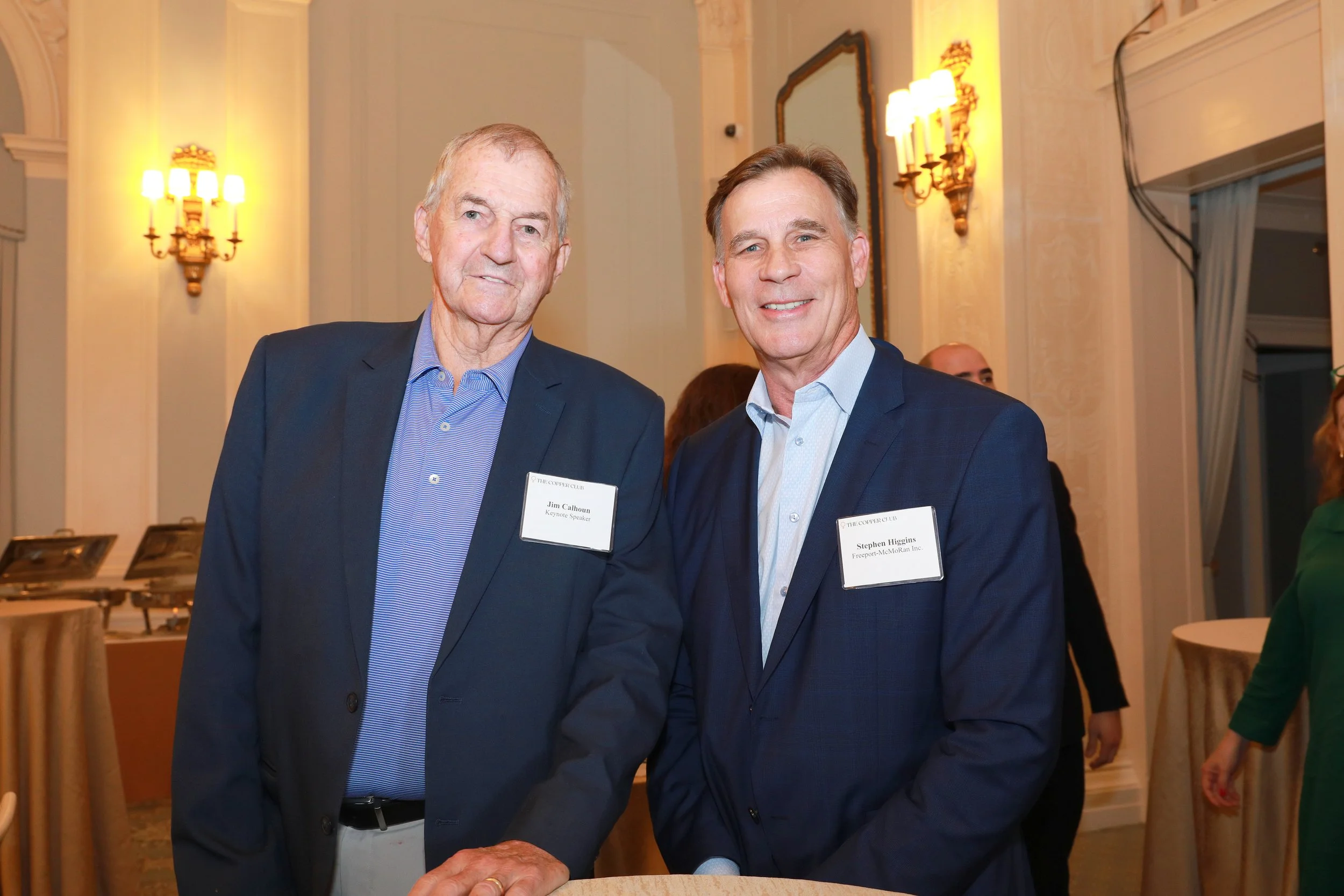 Two men dressed in suits smiling at an event, with name tags that read Jim Calhoun and Stephen Higgins.