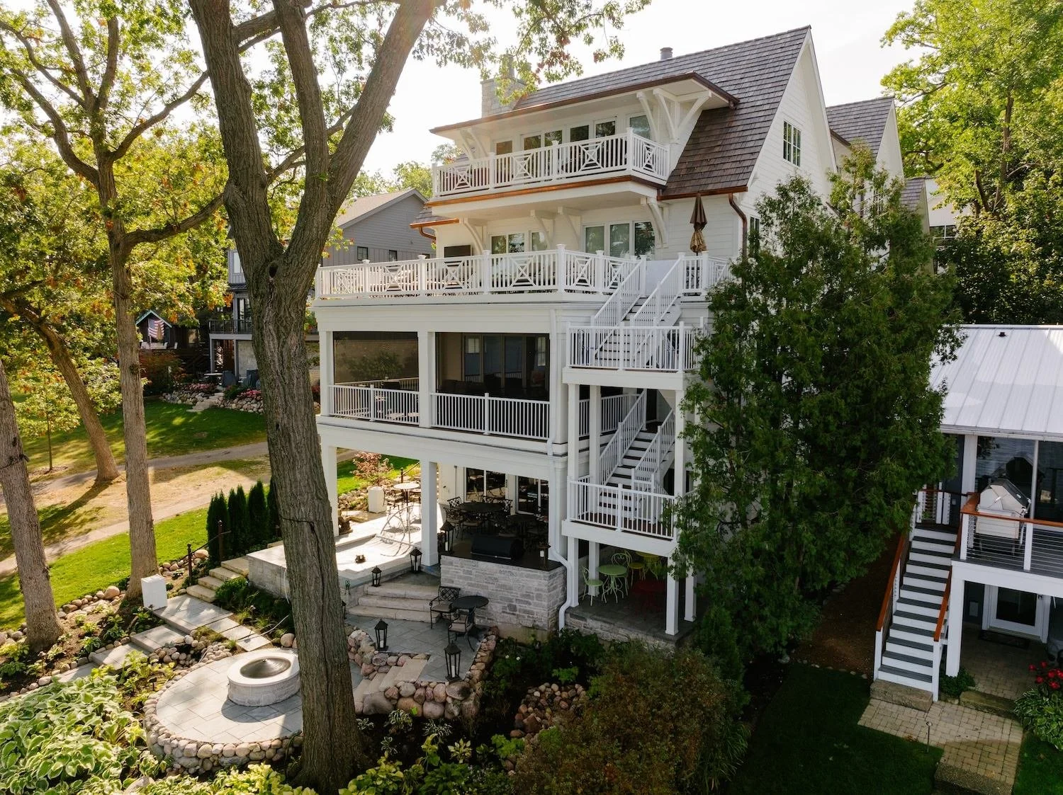 Aerial view of a lakefront home with a stone fire pit patio and terraced gardens by ILT Vignocchi