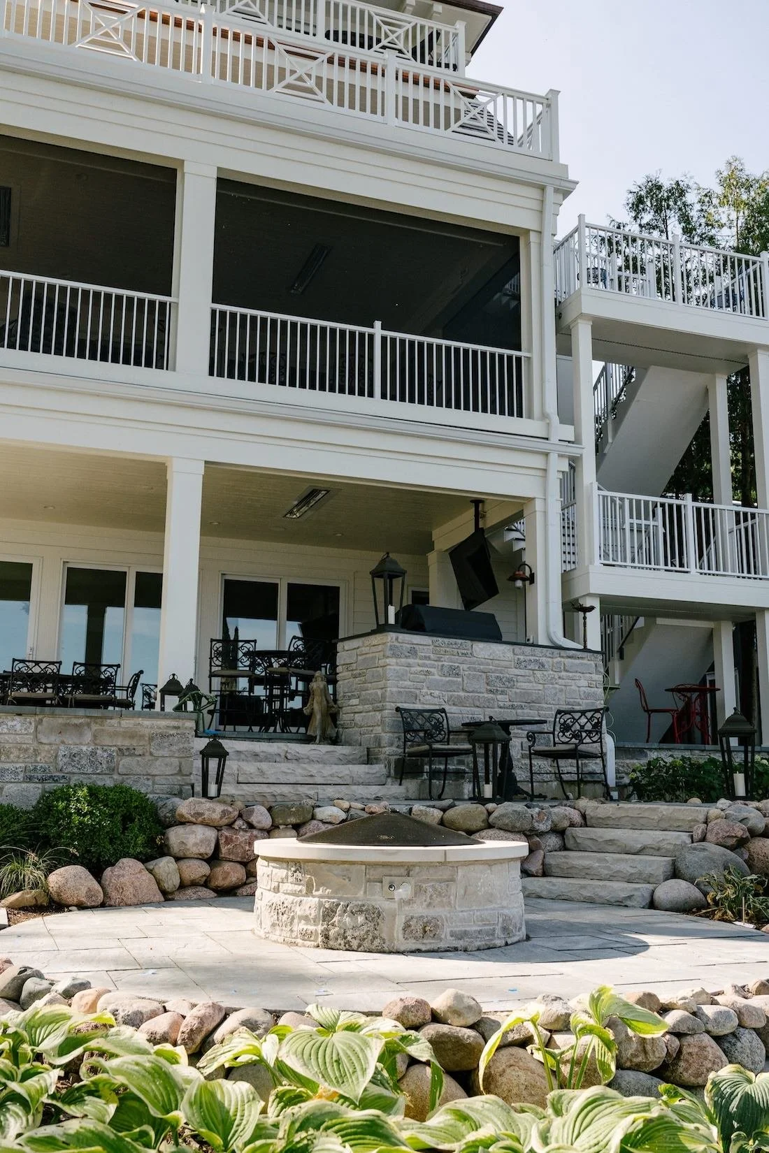 Multi-story house with outdoor balconies, patio furniture, a fire pit, and landscaping with rocks and green plants.