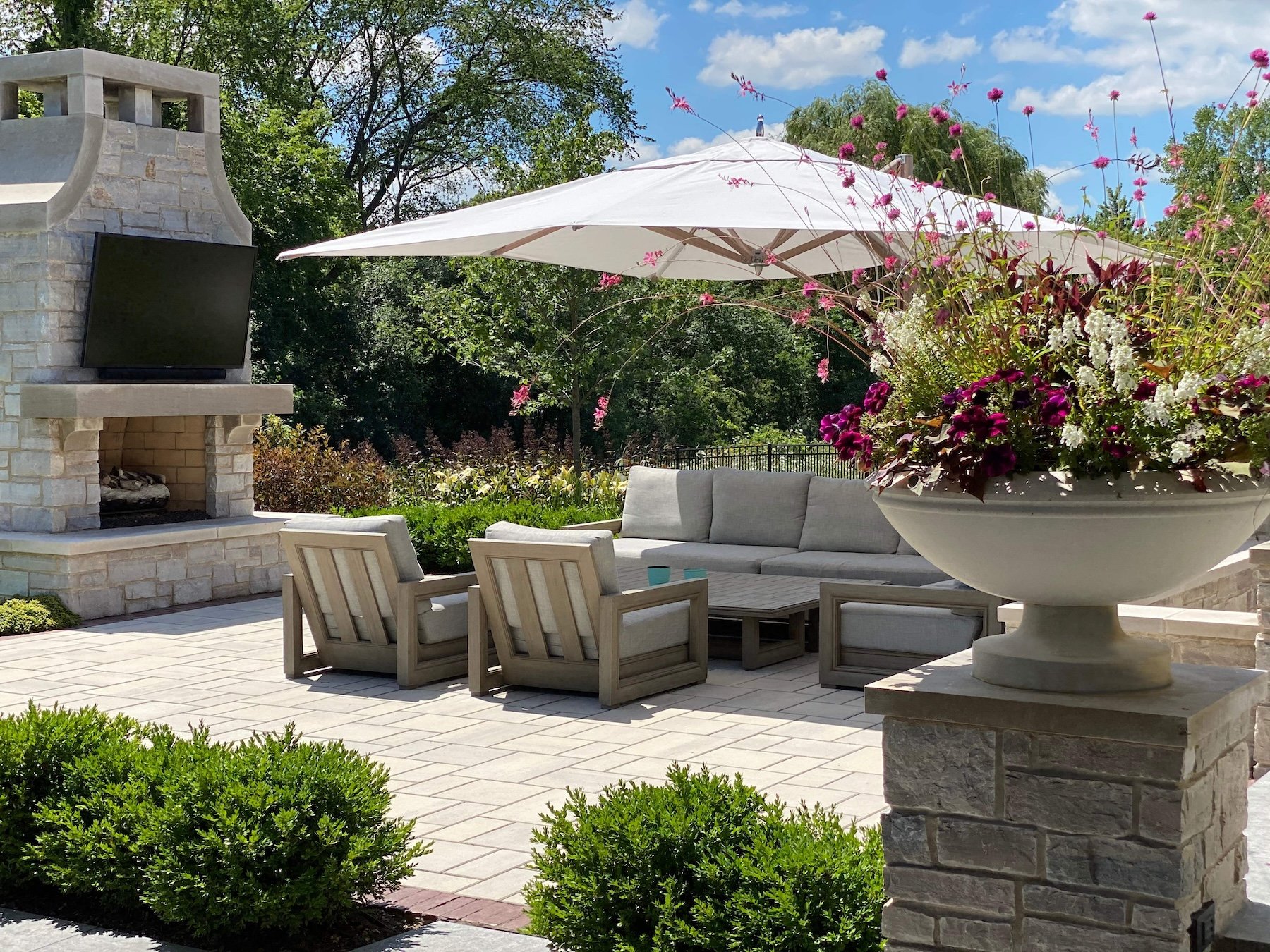 Paver patio with a stone outdoor fireplace, cushioned lounge seating, and a stone urn planter in Long Grove, Illinois