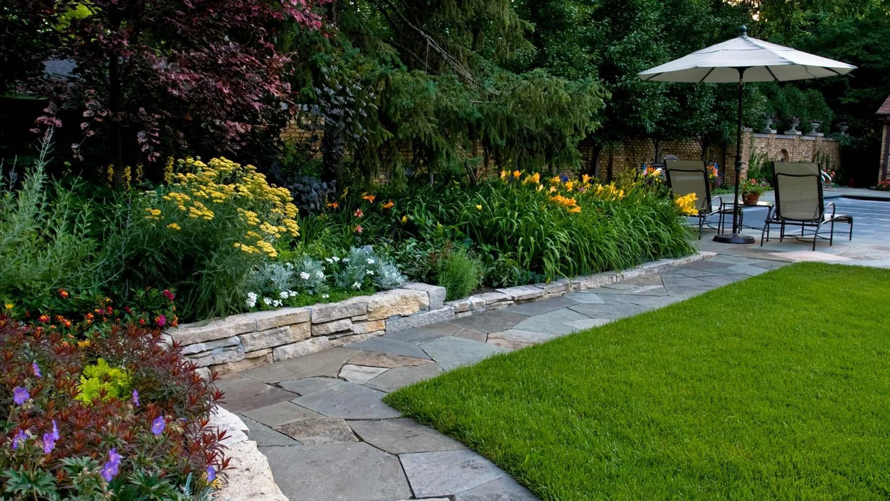 Flagstone walkway and stone-edged perennial garden bed beside a manicured lawn in Long Grove, Illinois