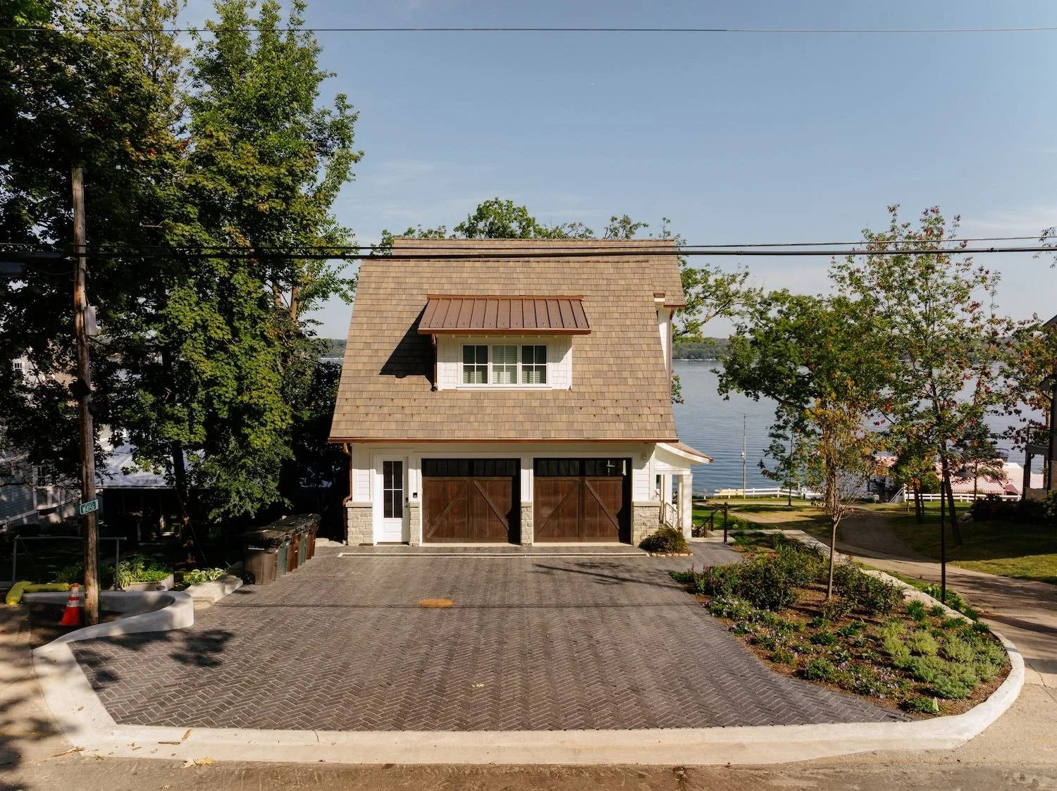 Front view of a two-story house with a garage, surrounded by trees and near a body of water.
