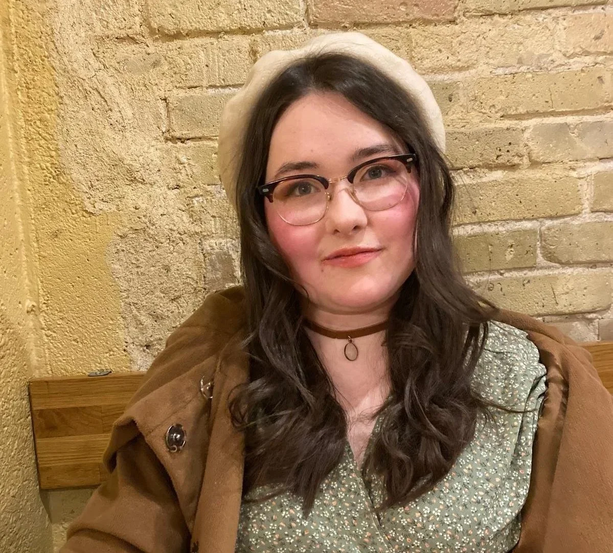 Profile photo of Maya in front of a brick wall.