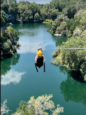Person ziplining over a lush green river surrounded by trees.