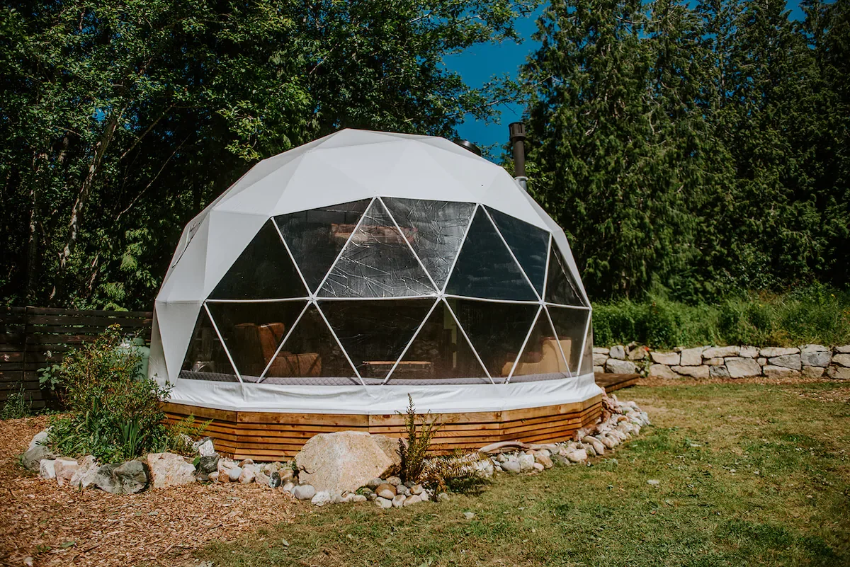 A geodesic dome tent in a garden with trees and rocks
