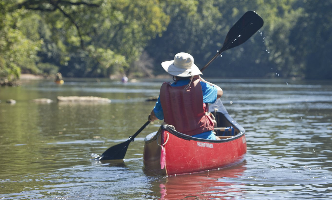 Person in red canoe paddling on a calm river surrounded by green trees