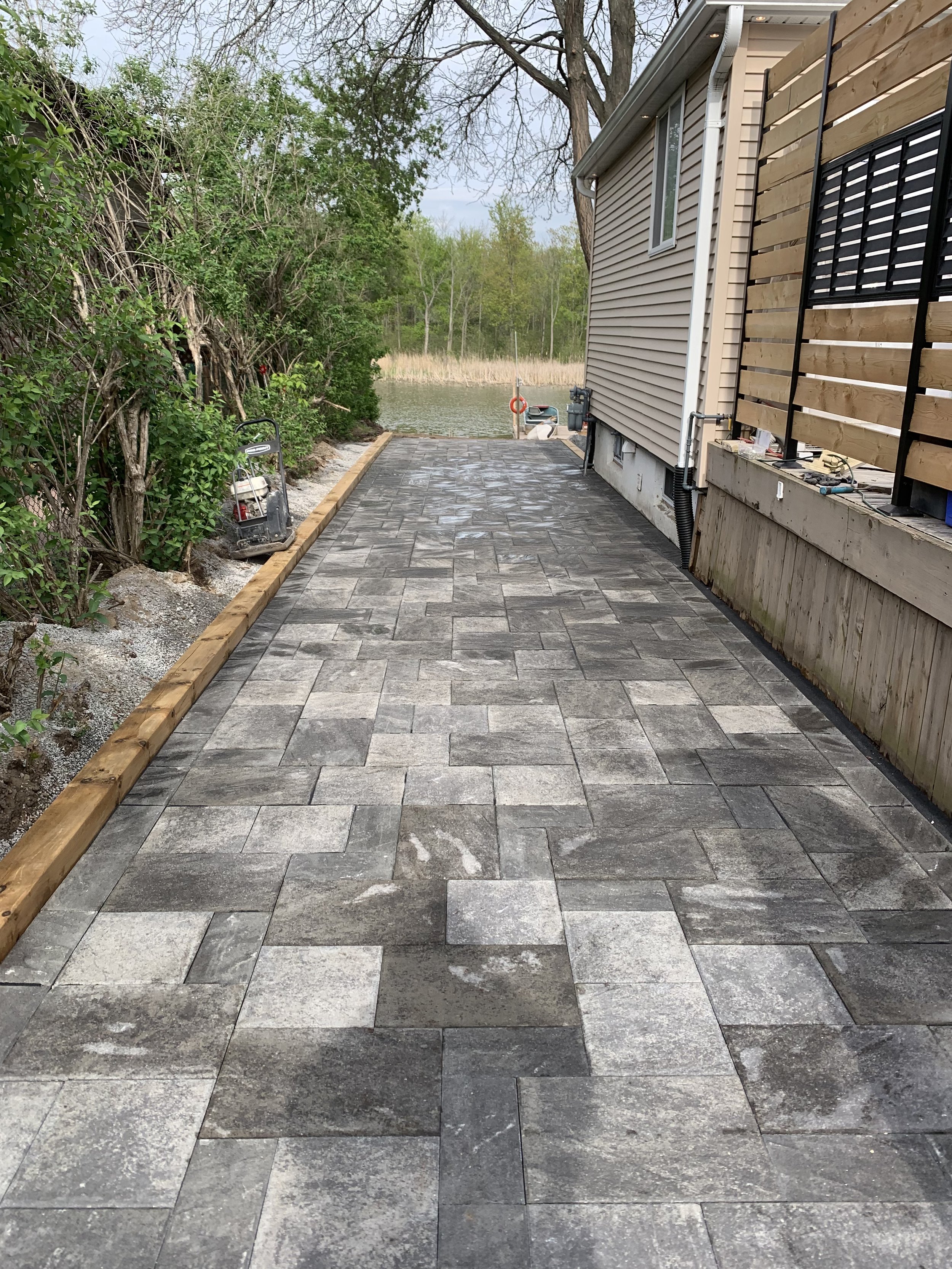 Patio area with new paver stones, wooden border, and a view of a lake with trees in the background.