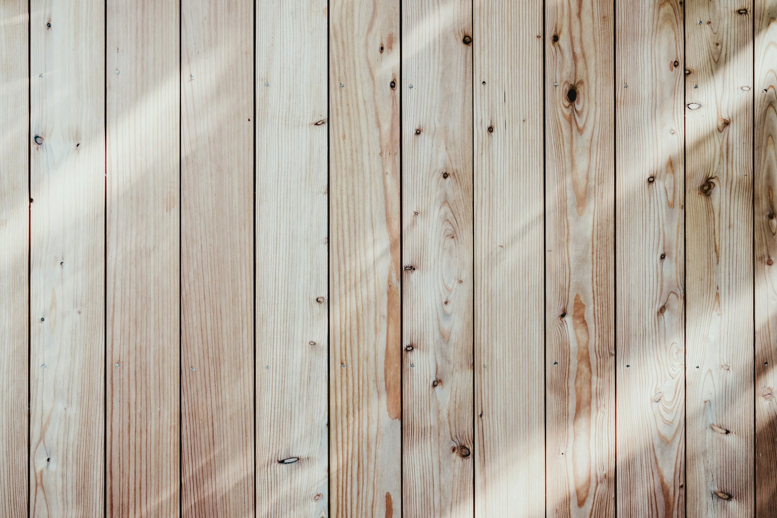 A close-up view of a light-colored wooden wall with vertically aligned planks, showing the wood grain and knots.