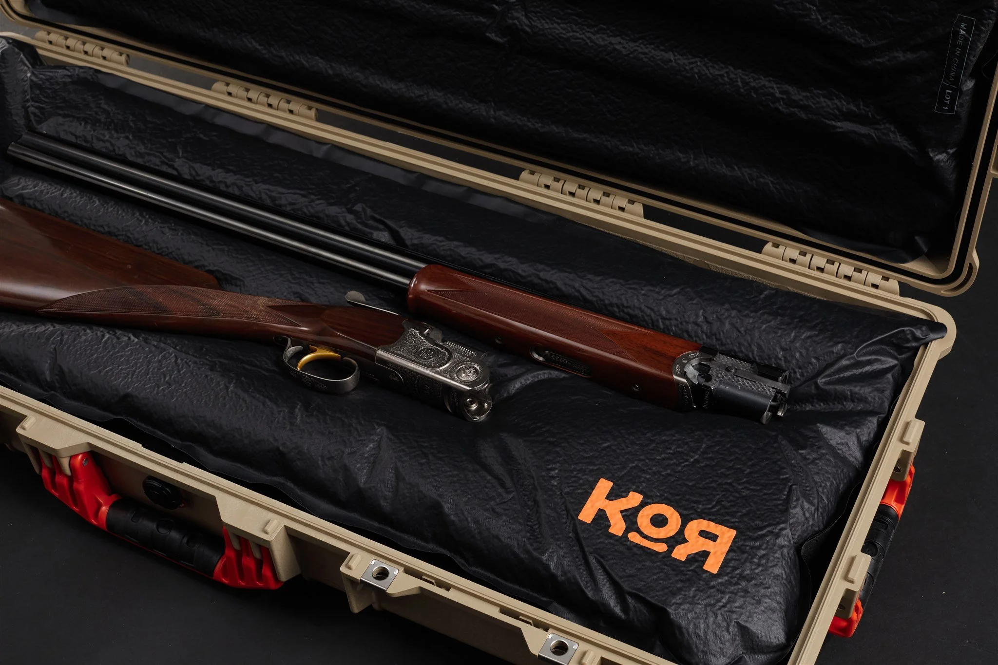 A gun case with a firearm and two long black rods inside, resting on a black cushioned surface with orange lettering.
