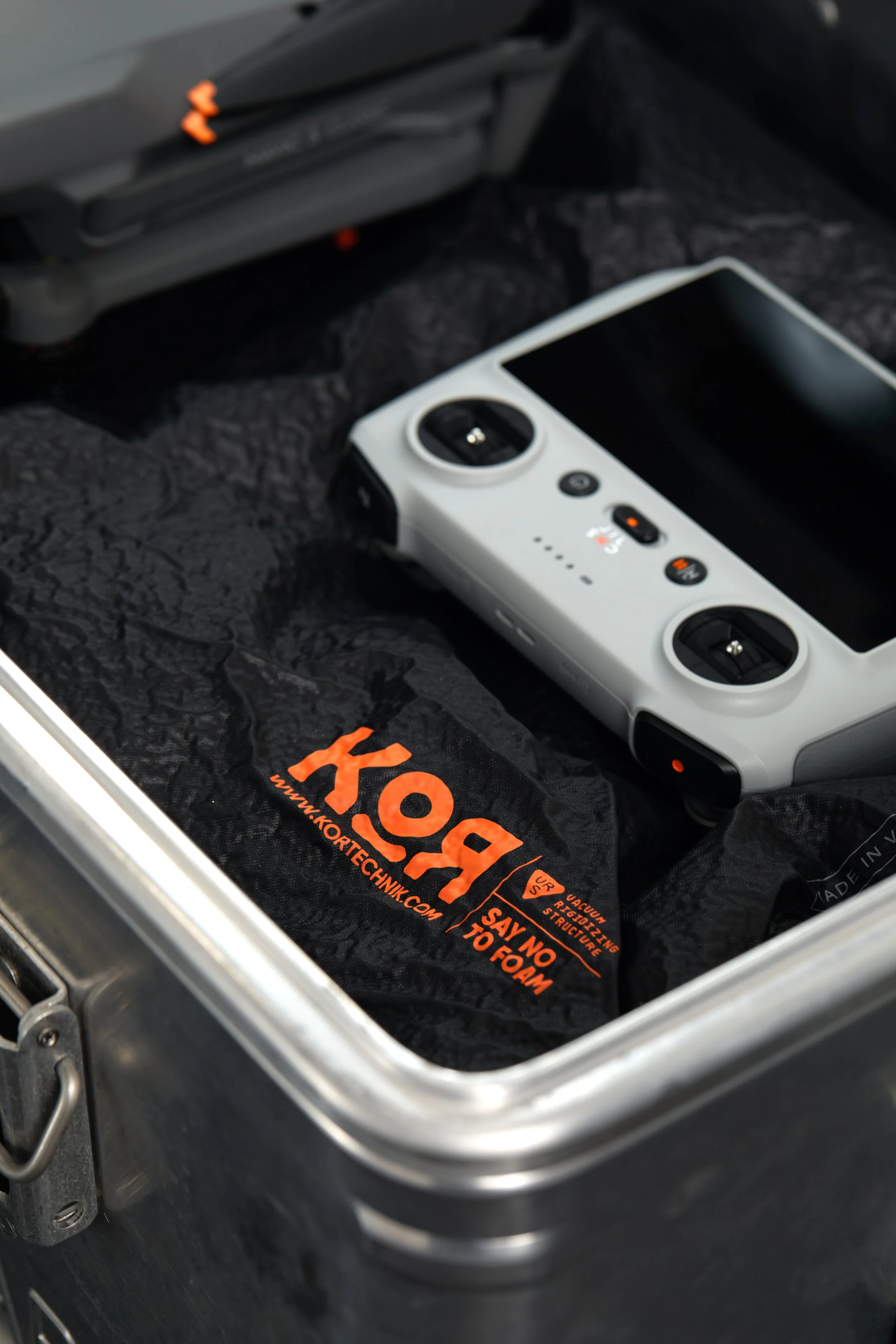 A polarized remote control with the kitchen engraving is placed inside a metal container, and a black foam under layer with orange text and website is visible beneath it.