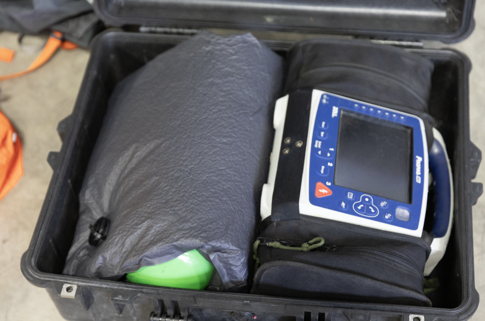 A black Pelican hard case containing a portable medical device with a blue and white display screen, a large KOR protection system panel, object wrapped in a black cover, and a green and white item, all inside a black Pelican case.