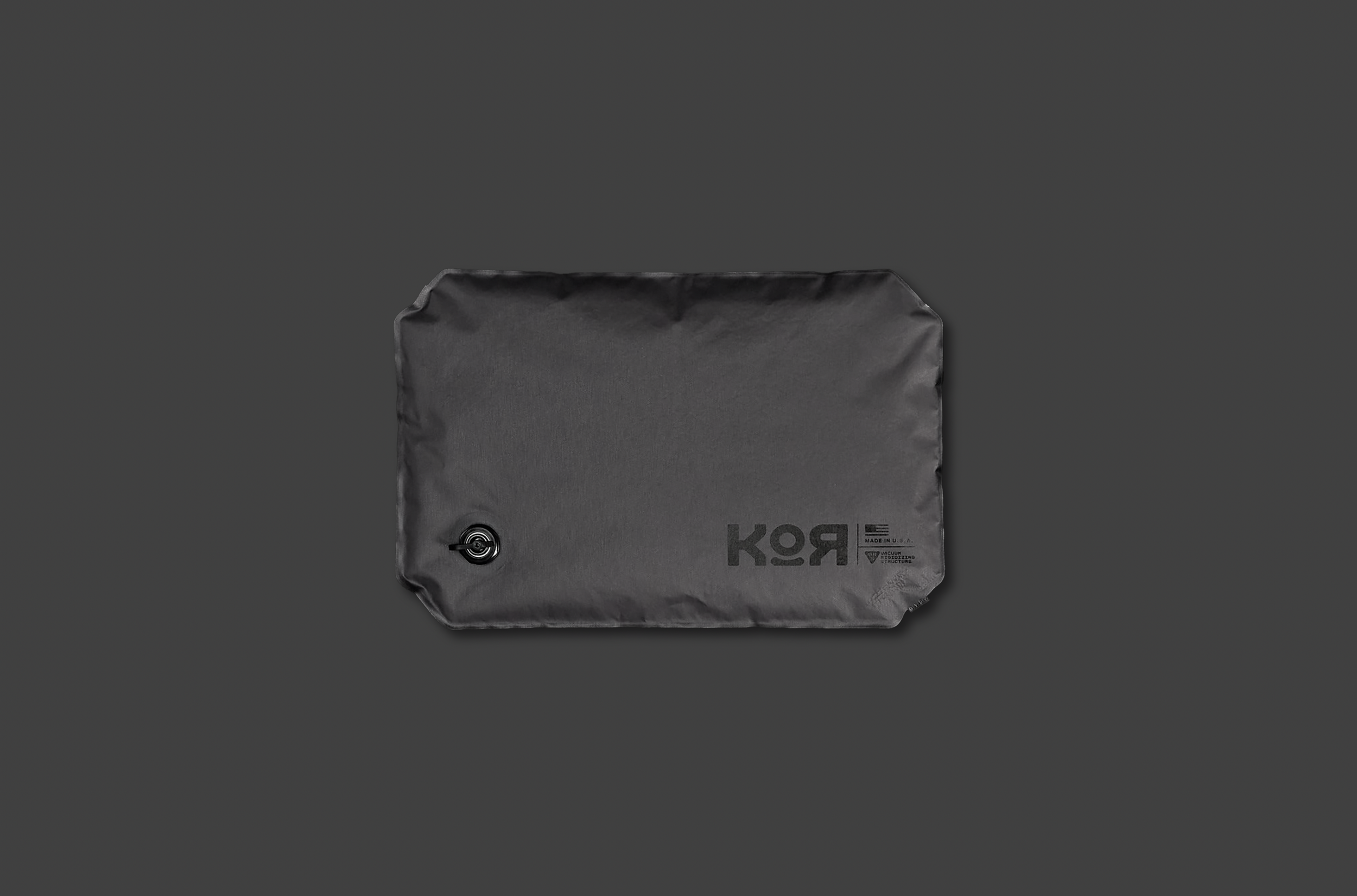 A black, rectangular vacuum storage bag with a circular valve on the lower left corner and the word "KOR" printed on it, placed on a dark gray background.