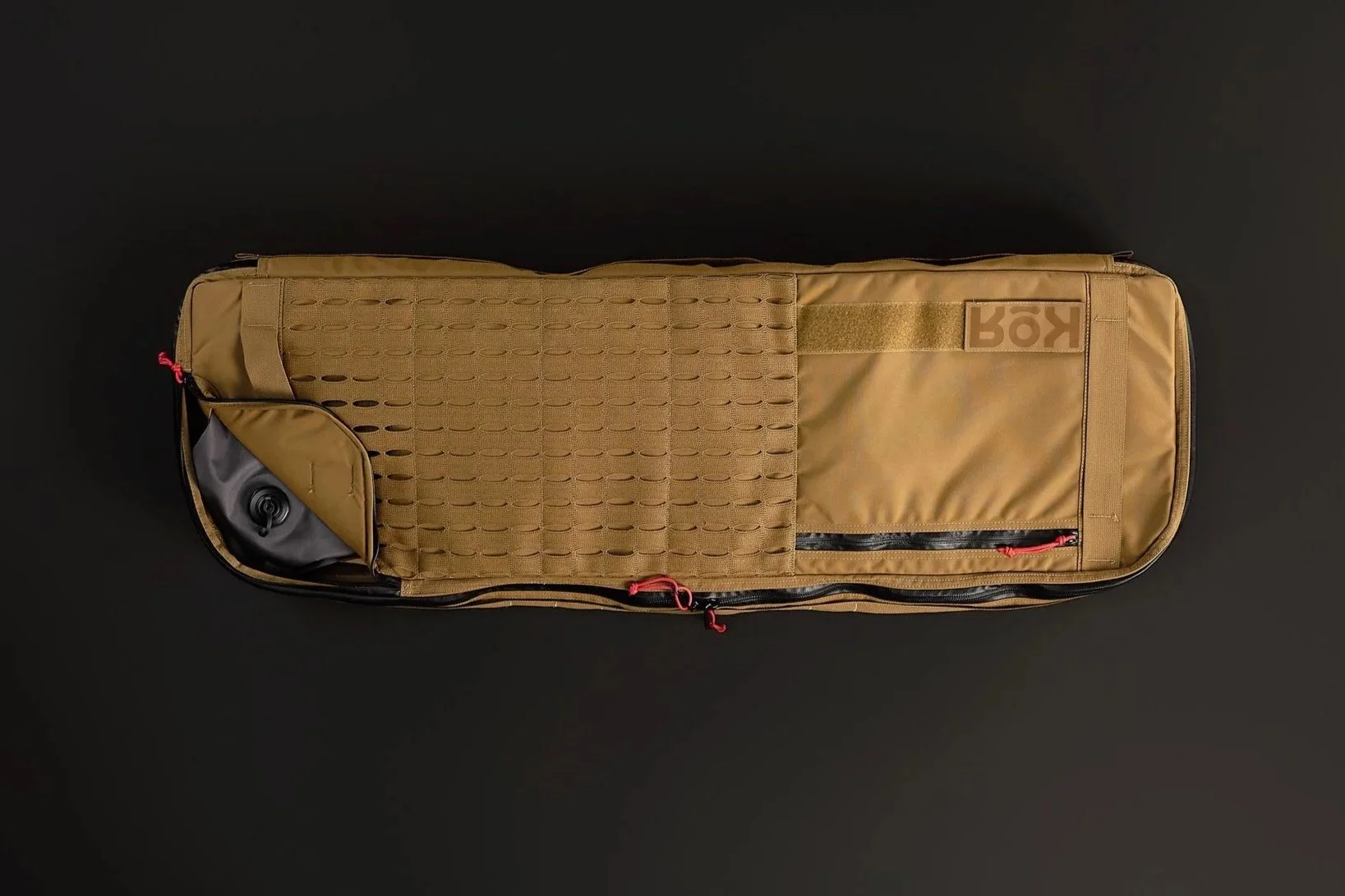 A tan rifle case with multiple compartments and zippers, lying on a black surface.