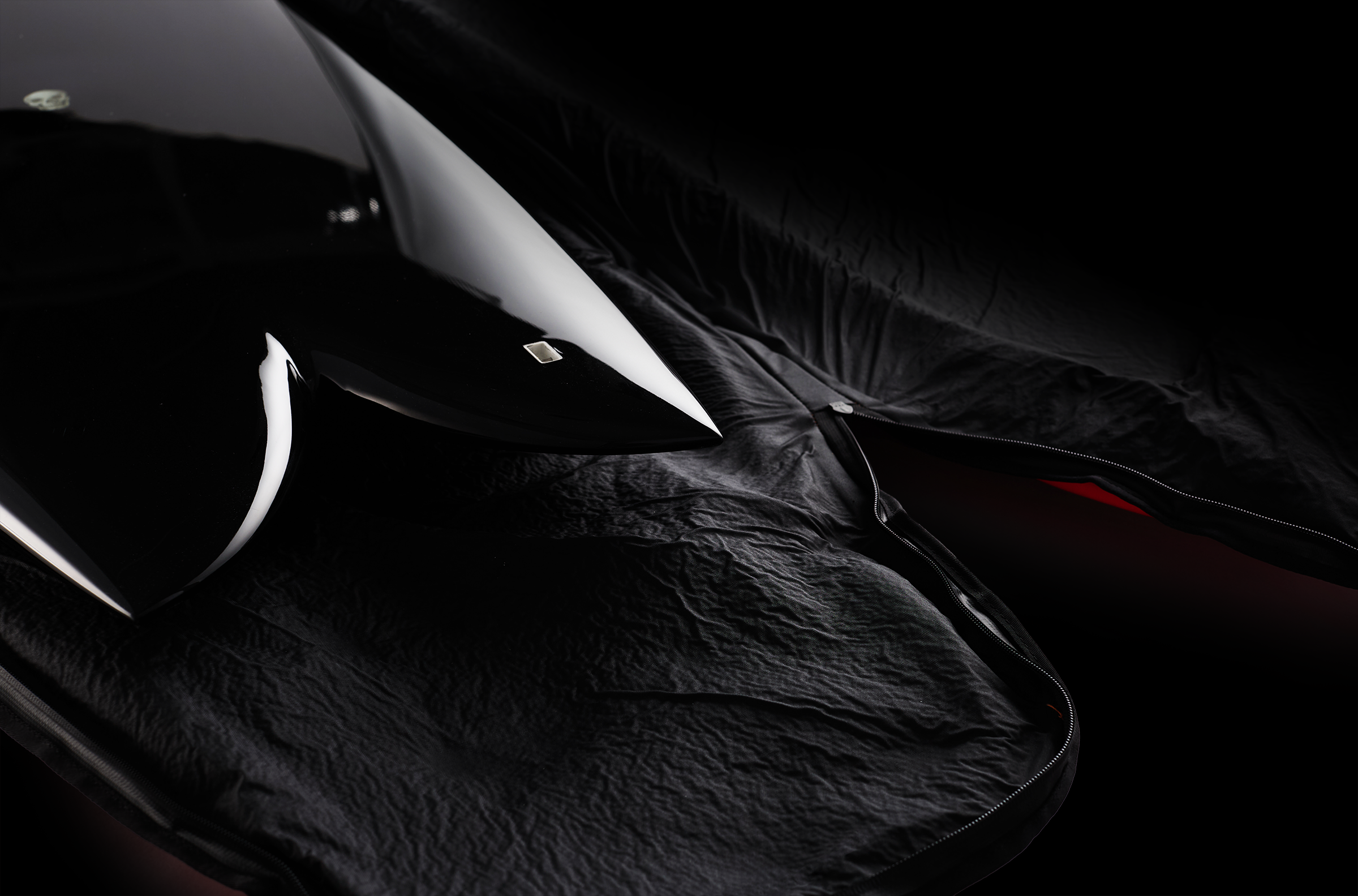 Close-up view of a black helmet resting inside a black padded bag with a zipper, on a black textured surface.