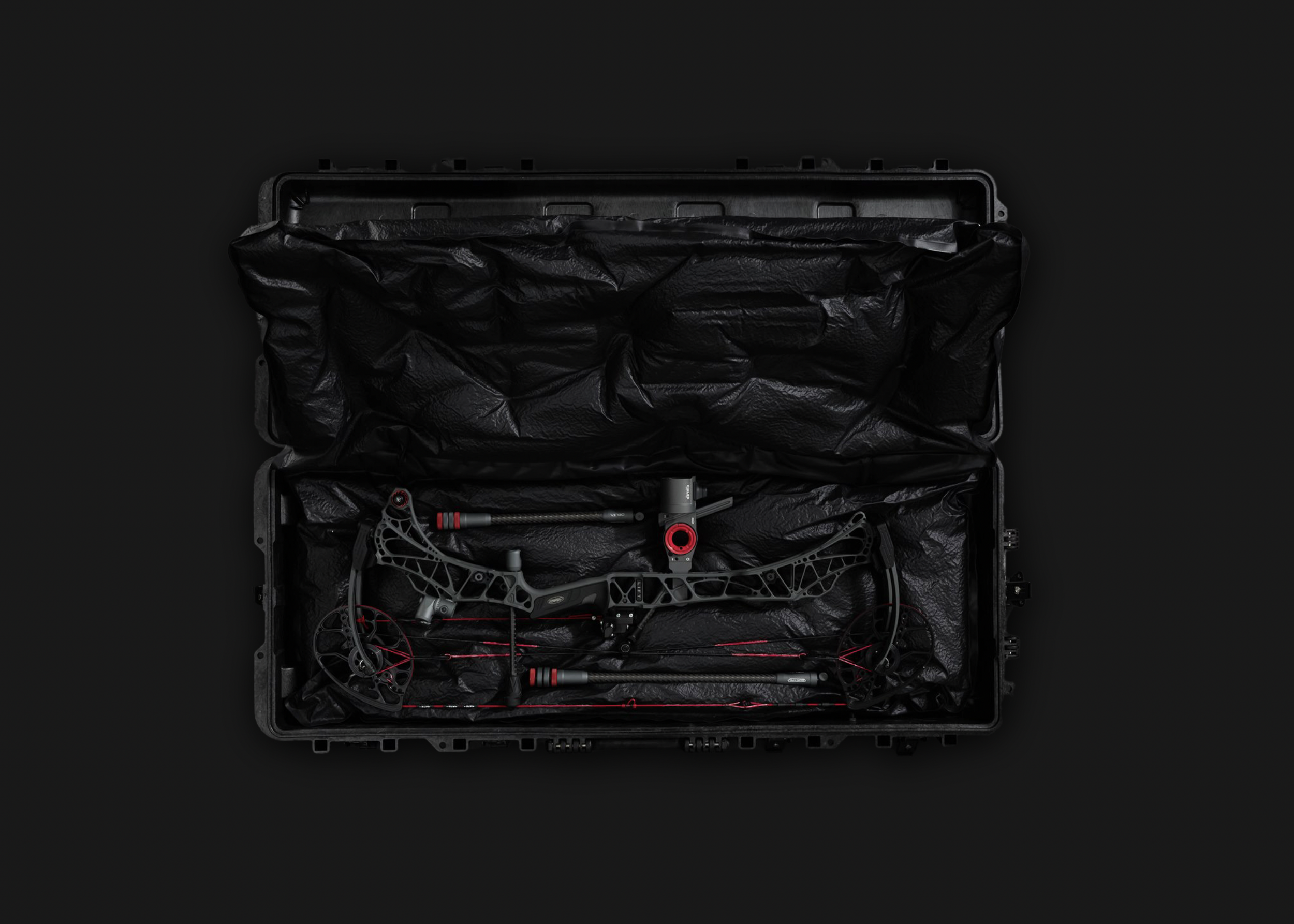 An open black hard case with foam padding, containing a modern compound bow with red and black accents, laid out for storage or transport.