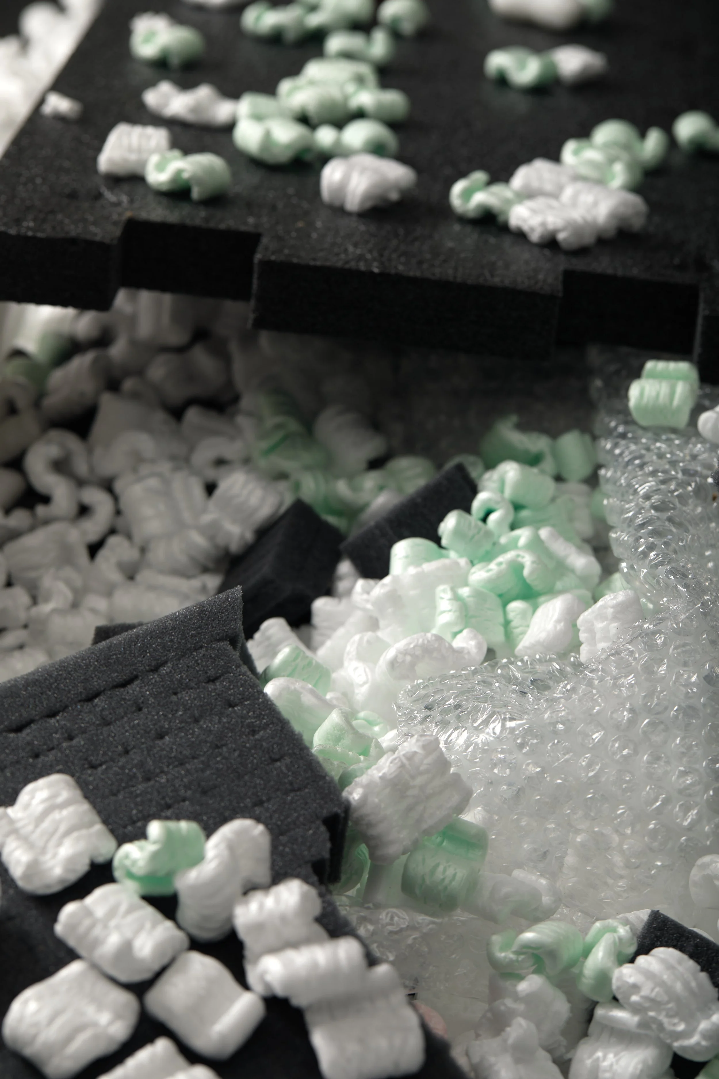 Close-up of a black foam meat tray filled with white and green packing peanuts and some crumpled white paper.