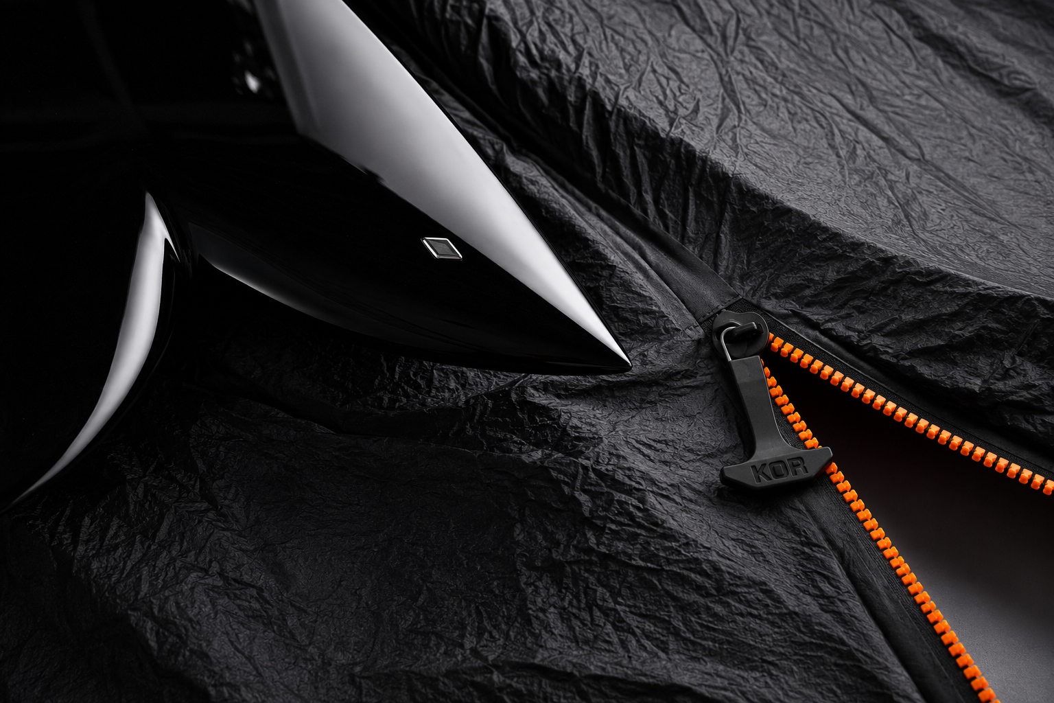 Close-up of a black and gray surfboard with a black and orange zipper on a black textured background.